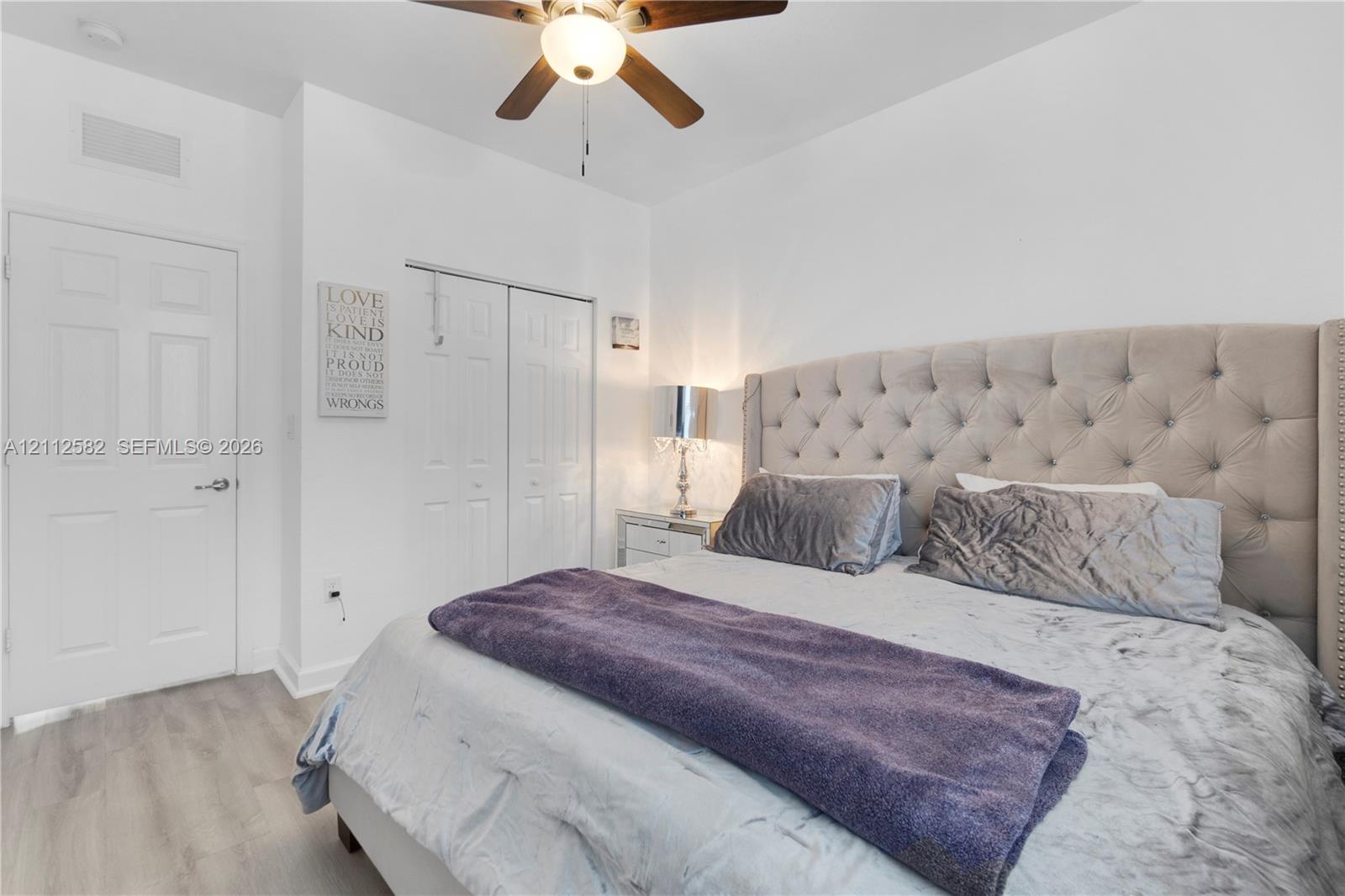 Wood-finish flooring, white panel door, double-door closet with bifold access, and a ceiling fan with integrated light fixture