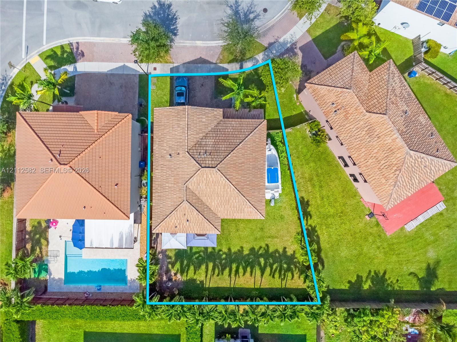 Aerial perspective of the property featuring a tiled hip roof, paved driveway, expansive lawn, and mature perimeter landscaping