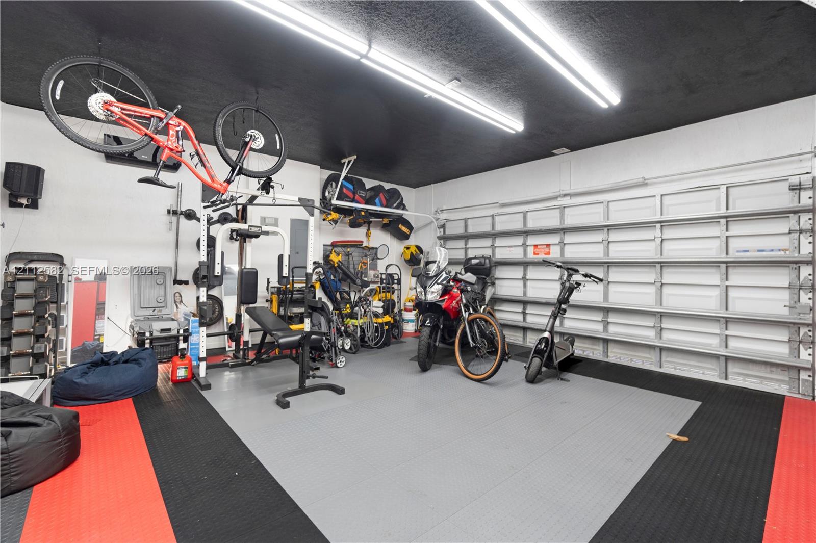 Garage space featuring modular interlocking floor tiles, dual overhead LED tube lighting, and a metal roll-up garage door