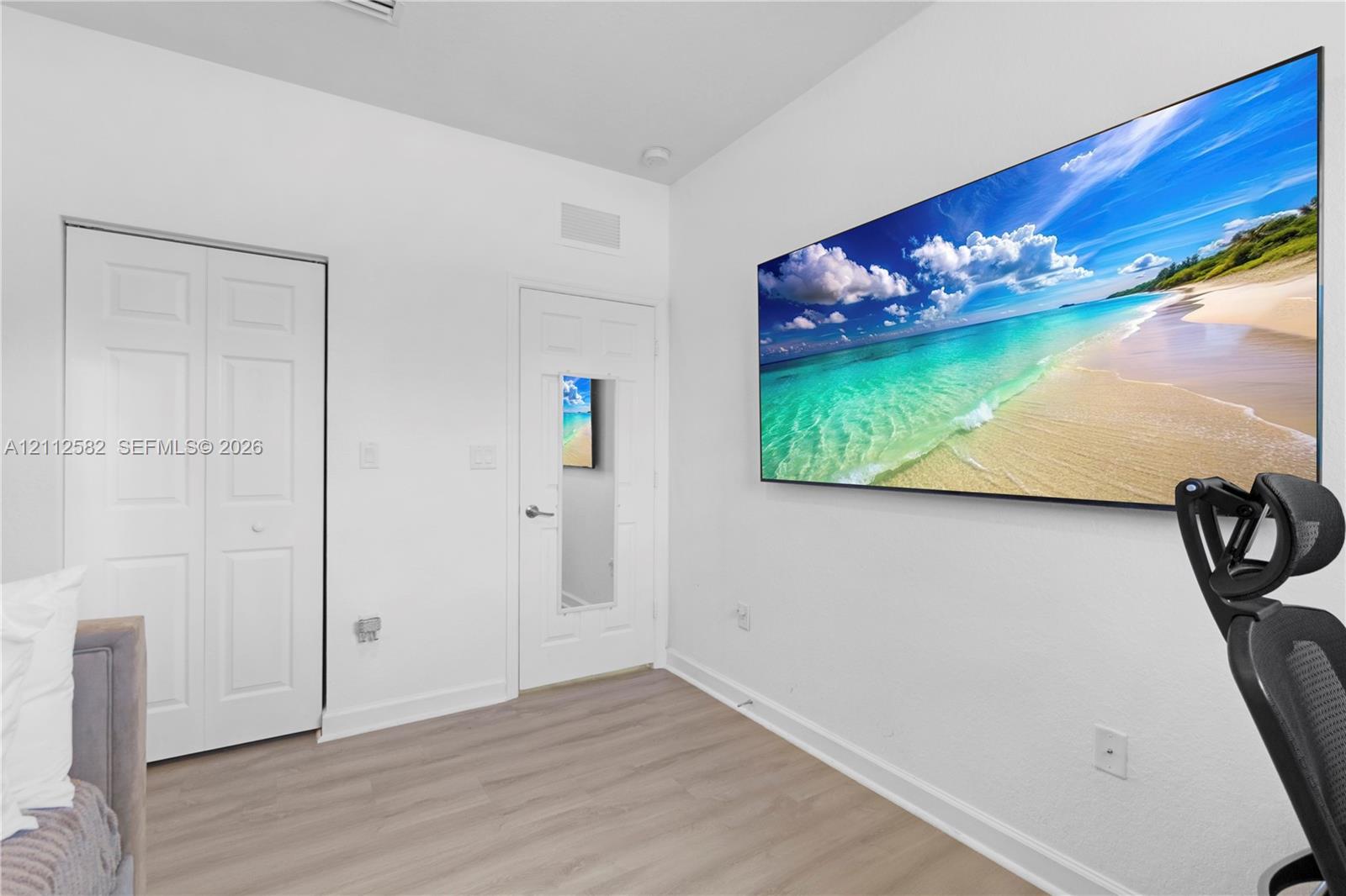 Interior room featuring wood-finish flooring, white walls, a double-door closet, and a single-panel door with an integrated mirror