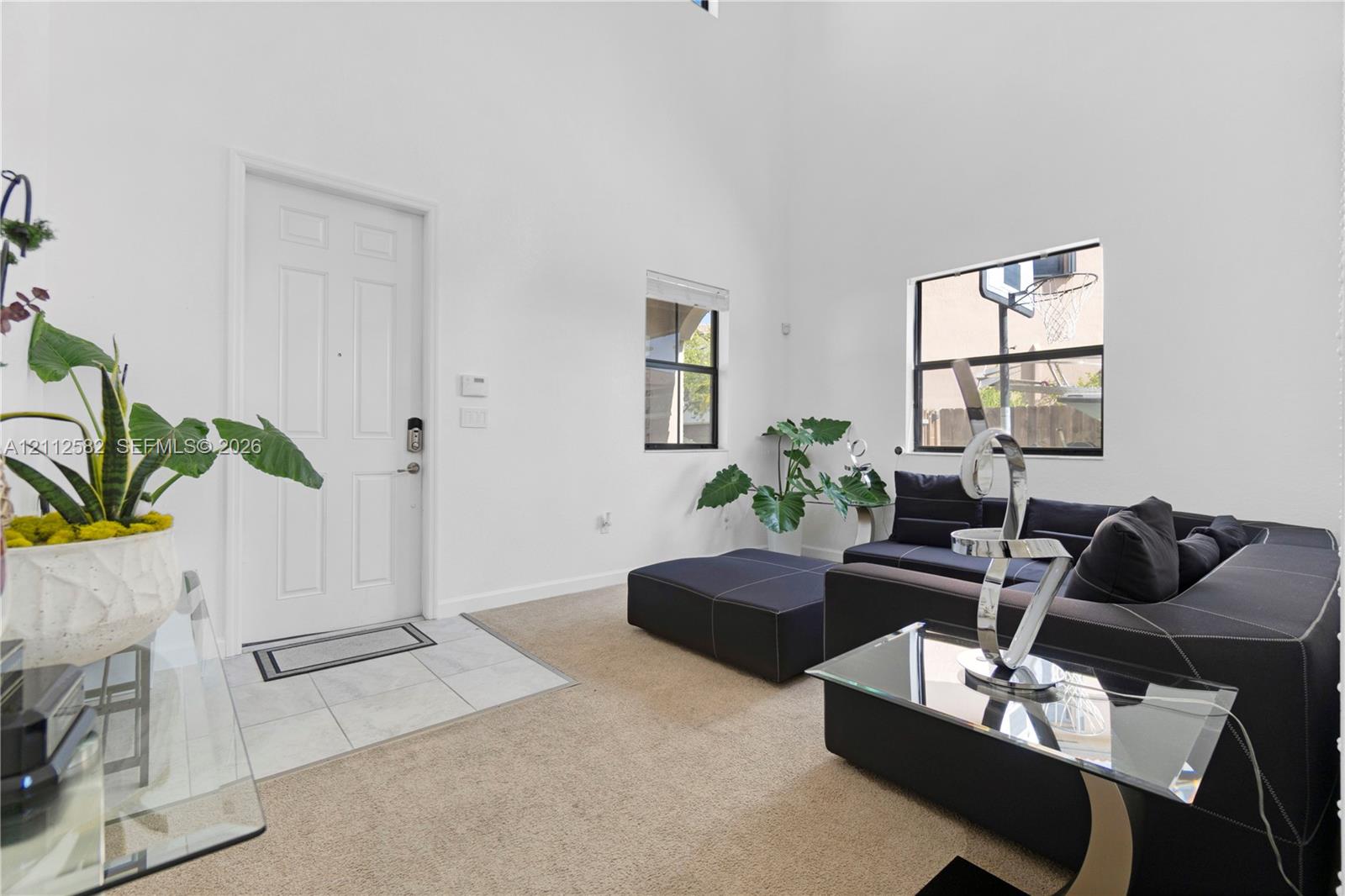 High-ceiling living area featuring neutral carpeting, ceramic tile entryway flooring, and large window placements