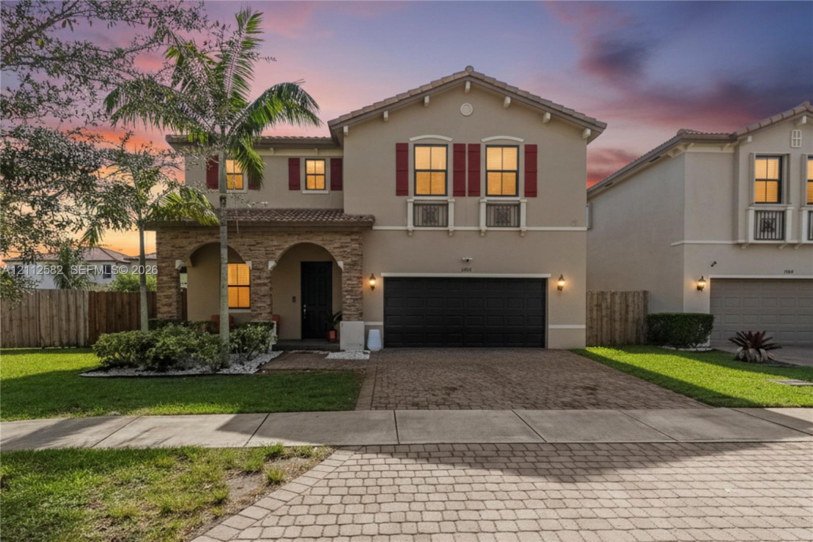Two-story exterior featuring a stone-veneer facade, arched entryway, paved driveway, and decorative window shutters