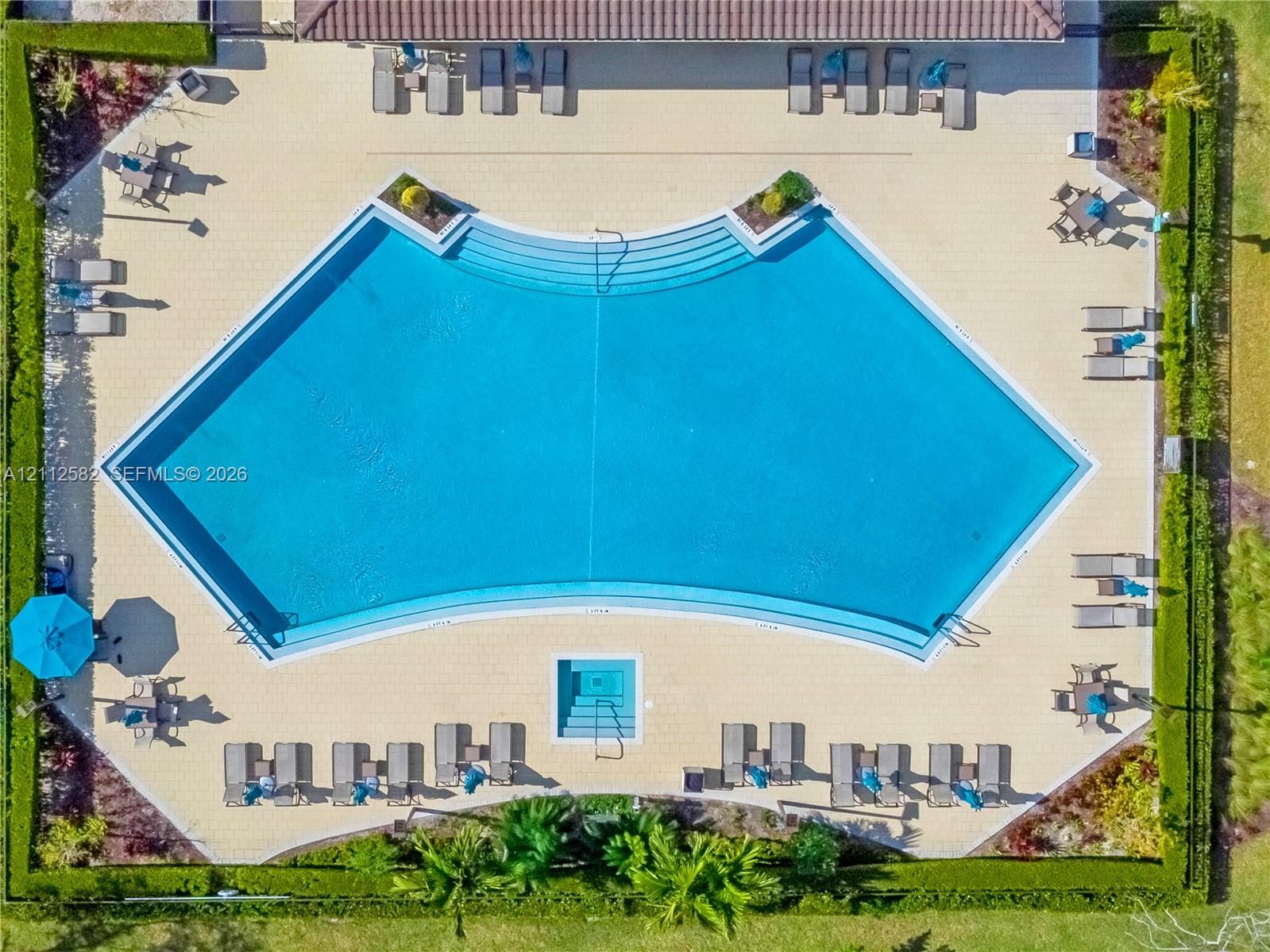 Swimming pool featuring a curved design, integrated stairs, an attached spa, and surrounding paved pool deck enclosed by manicured privacy hedging
