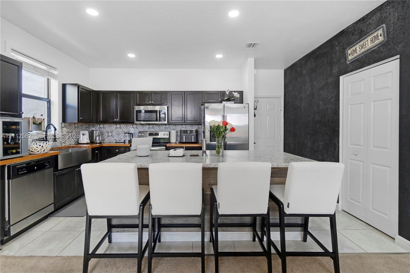 Kitchen featuring dark wood cabinetry, stainless steel appliances, patterned tile backsplash, oversized stone-topped island, and recessed lighting Kitchen featuring dark wood cabinetry, stainless steel appliances, patterned tile backsplash, oversized stone-topped island, and recessed lighting