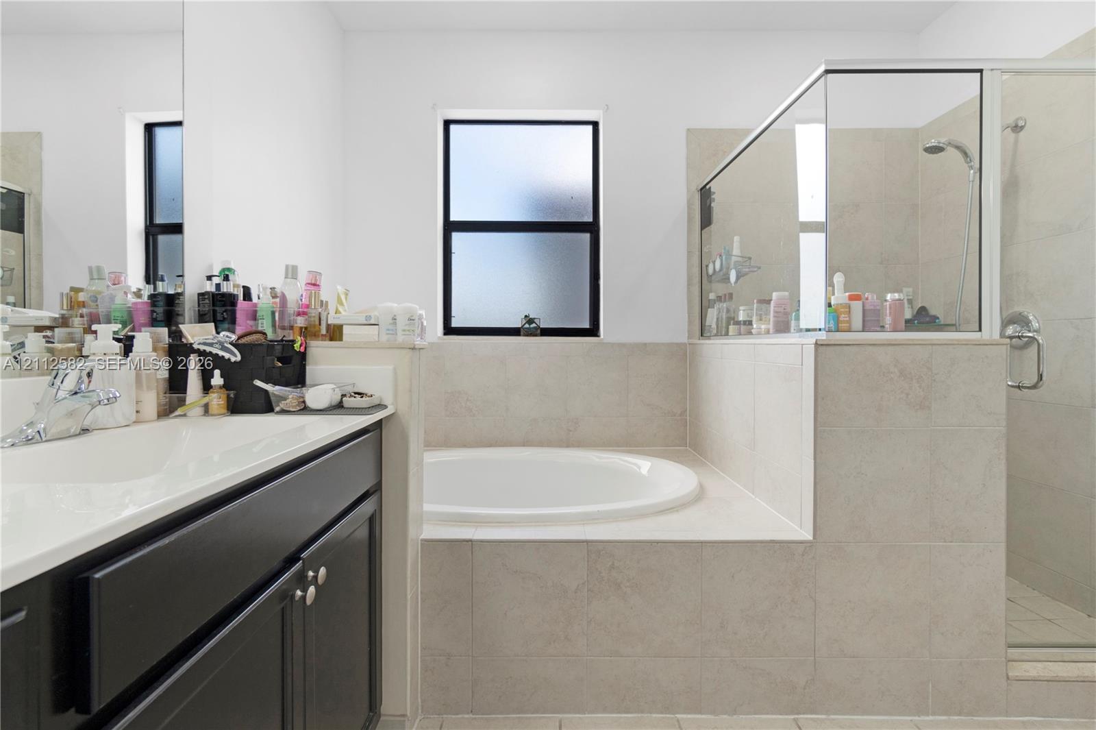 Bathroom featuring a dark wood-finish vanity, solid-surface countertop with an integrated basin, a large soaking tub, and a walk-in shower with tile surround and glass enclosure