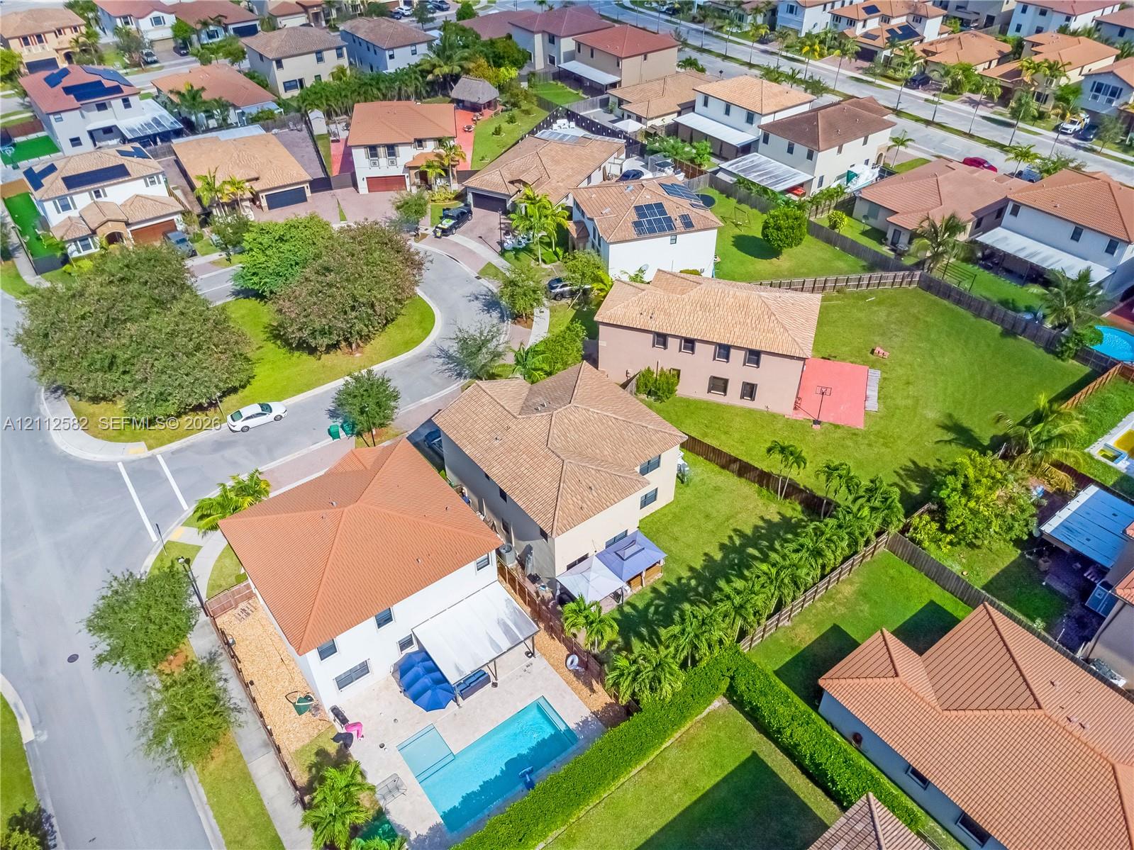 Aerial perspective of a multi-story residence featuring a rectangular swimming pool, concrete pool deck, and perimeter fencing Aerial perspective of a multi-story residence featuring a rectangular swimming pool, concrete pool deck, and perimeter fencing