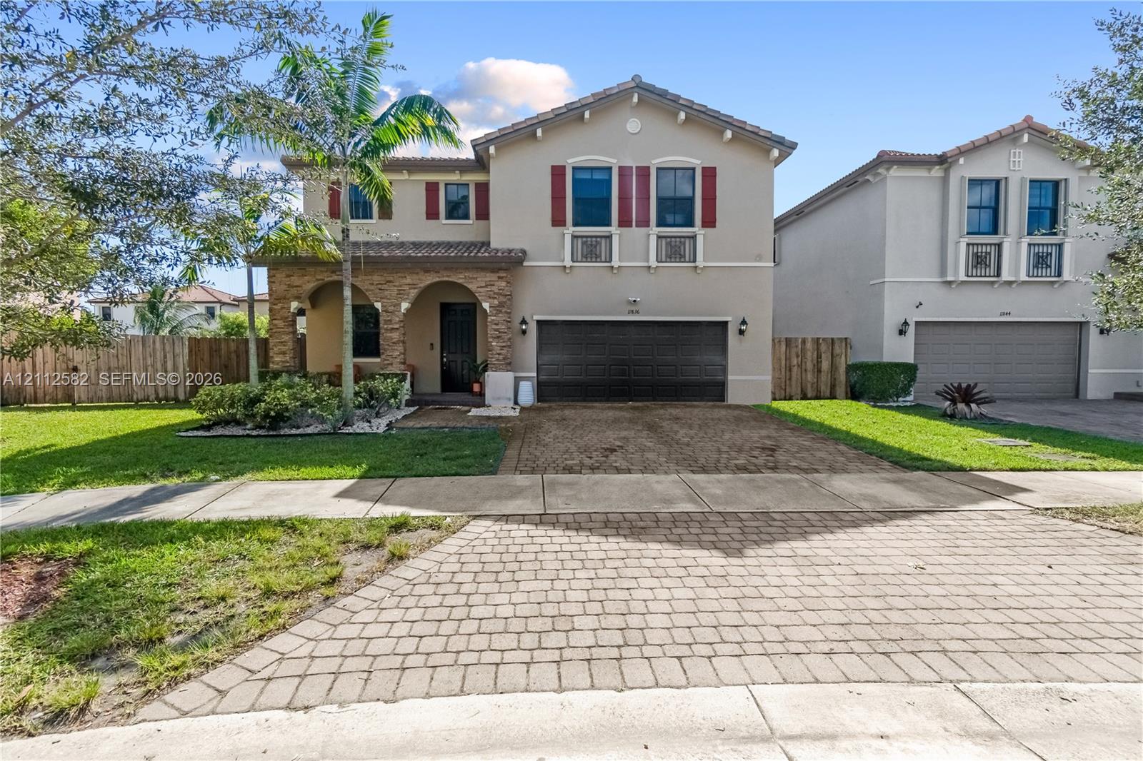 Two-story residence featuring a stone-clad arched entryway, paver driveway, decorative window shutters, and a multi-car garage Two-story residence featuring a stone-clad arched entryway, paver driveway, decorative window shutters, and a multi-car garage
