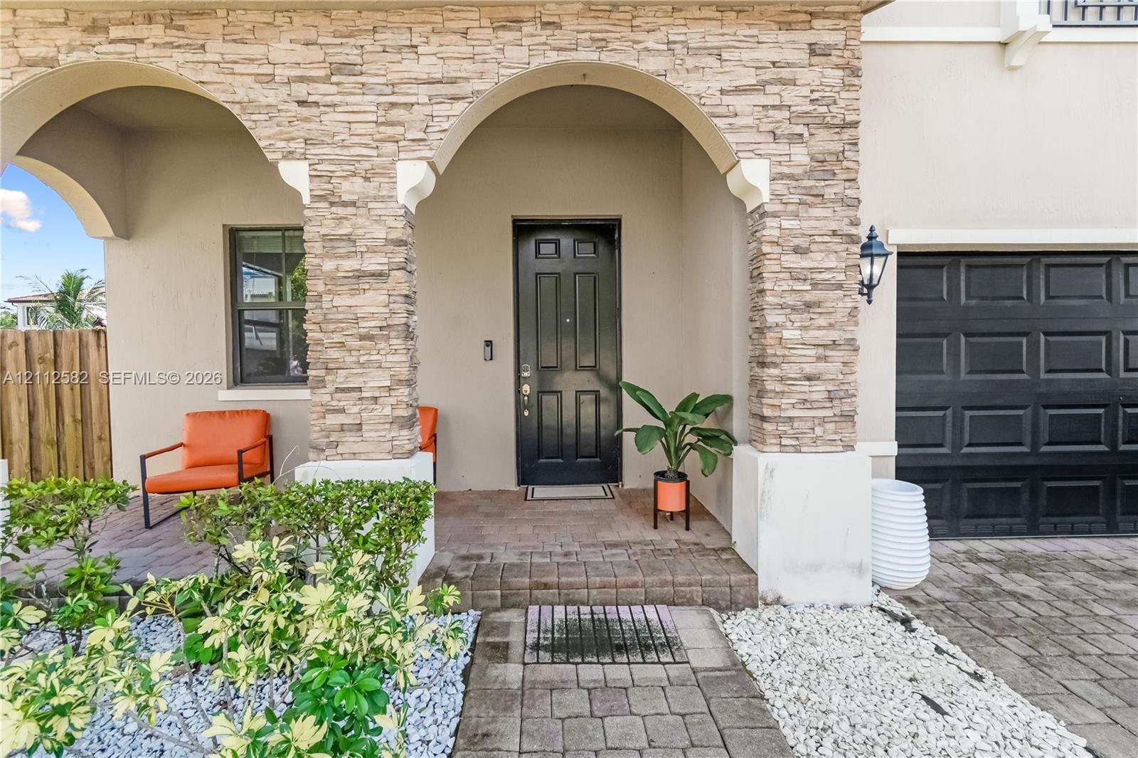 Exterior entry featuring stacked stone pillars, arched portico, paver walkway, and dark-toned entry door and garage Exterior entry featuring stacked stone pillars, arched portico, paver walkway, and dark-toned entry door and garage