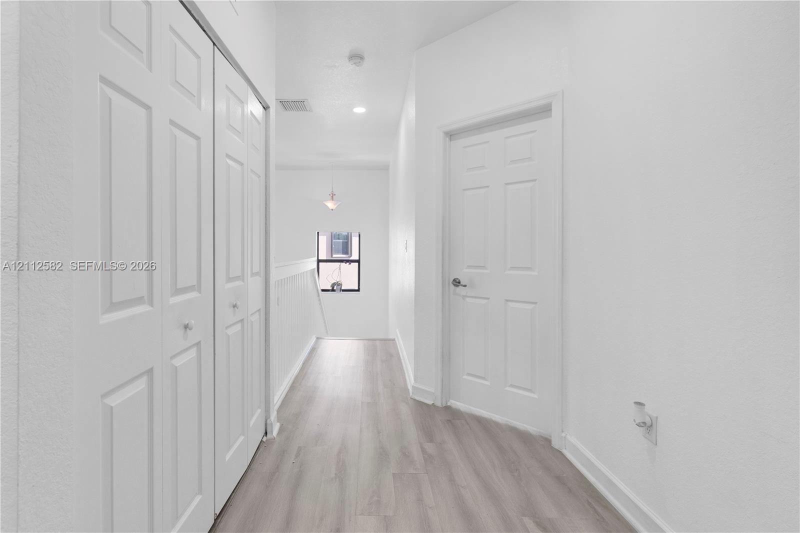 Hallway featuring wood-finish flooring, white six-panel interior doors, recessed lighting, and a bi-fold closet