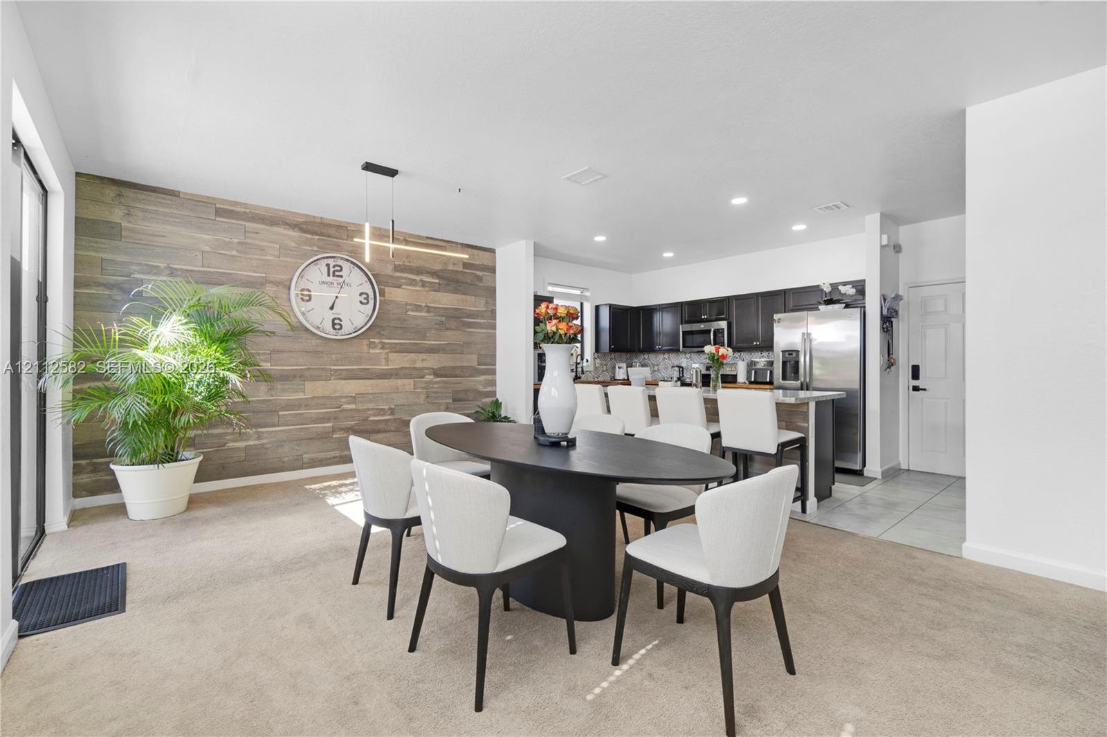 Open-concept area featuring a rustic wood-plank accent wall, recessed lighting, and a breakfast bar with built-in cabinetry and stainless steel appliances