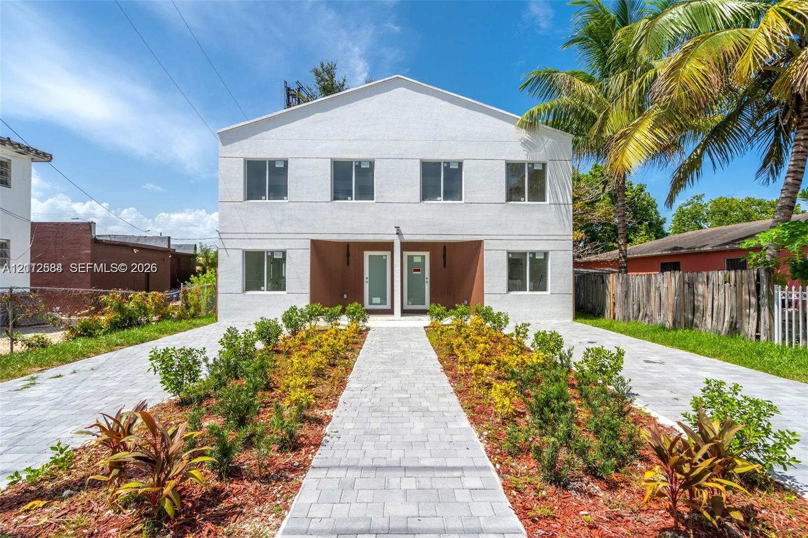 Two-story exterior featuring a white stucco facade, paved walkways, landscaped garden beds, and dual entry points