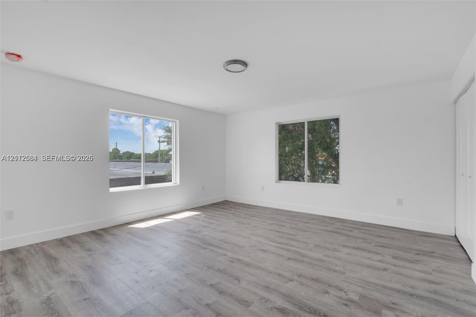 Spacious room featuring wood-finish flooring, dual windows, neutral wall tones, and built-in closet cabinetry