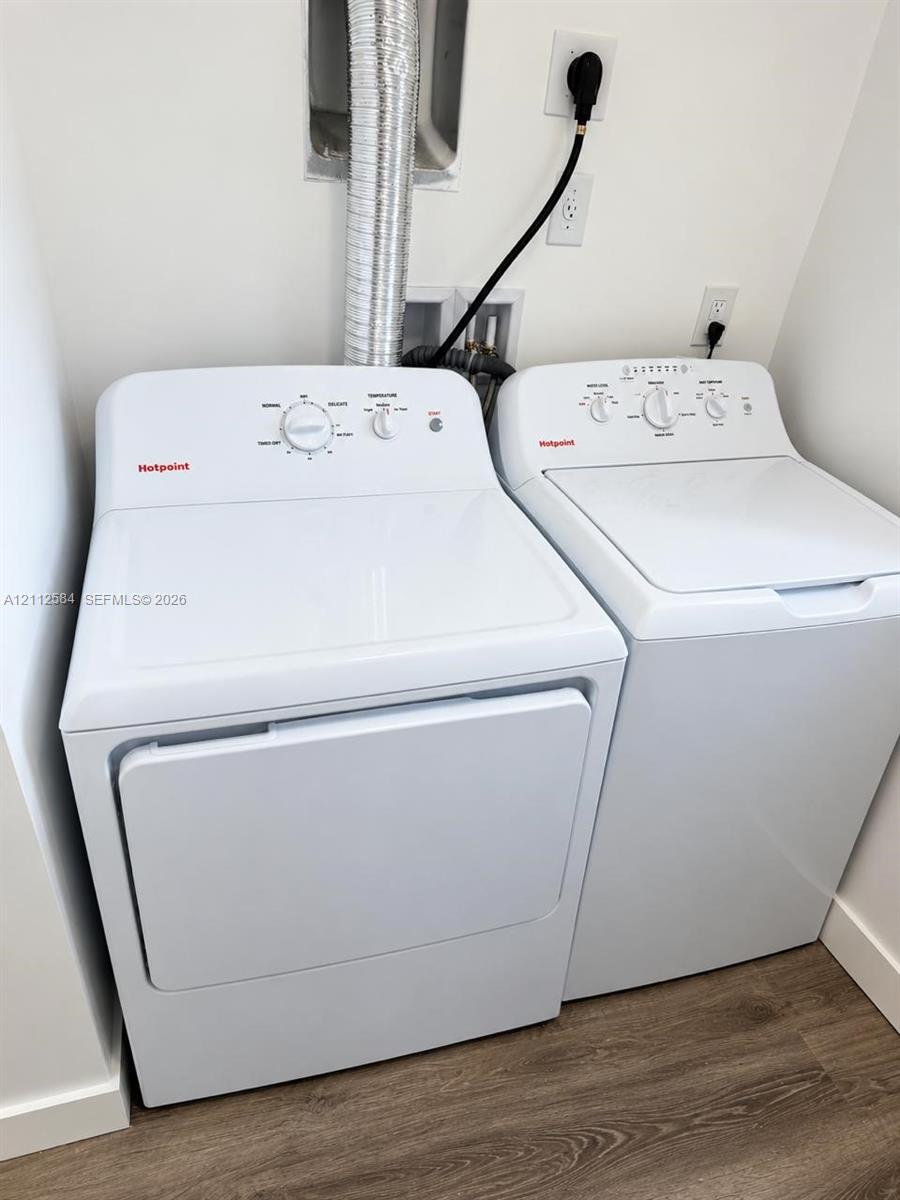 Laundry area equipped with a top-load washing machine, front-load electric dryer, and wood-finish flooring
