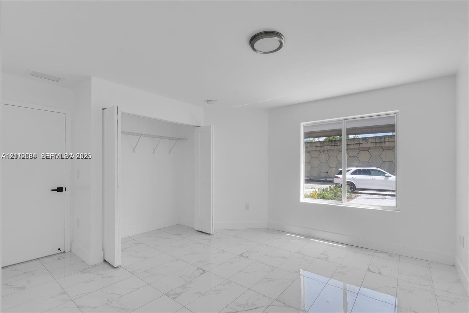 Interior space featuring neutral wall paint, large-format tile flooring, a closet with built-in shelving, and a large window