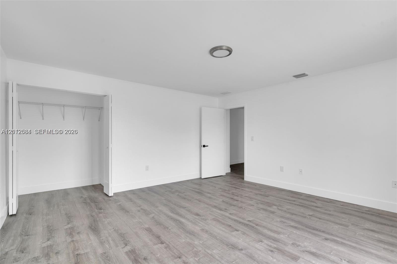 Neutral-toned wood-finish flooring, white walls, and built-in closet storage featuring double-hinged doors and a ceiling-mounted light fixture