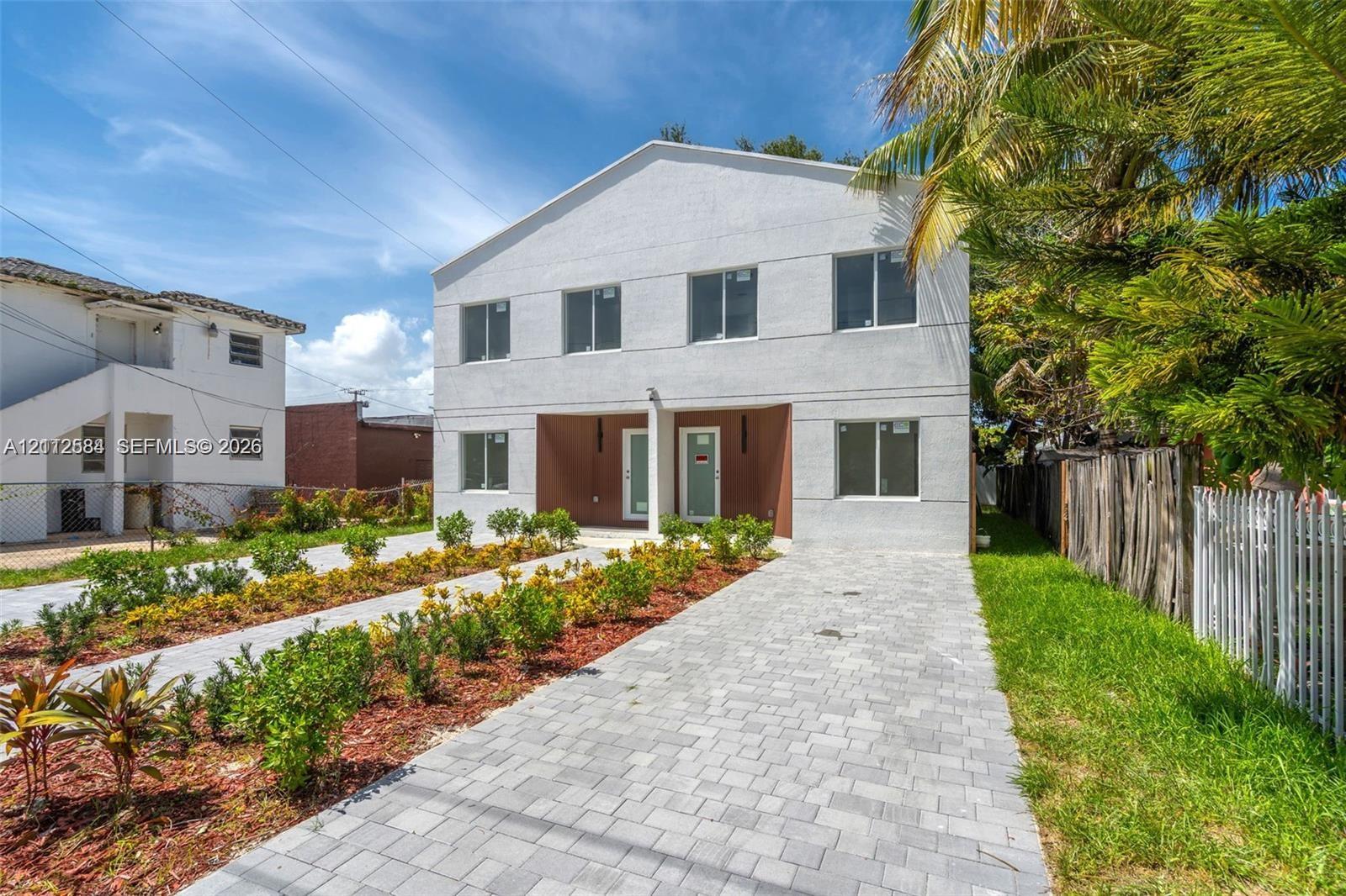 Two-story exterior featuring a light-toned stucco facade, dual recessed entryways, rectangular windows, and a paved stone driveway