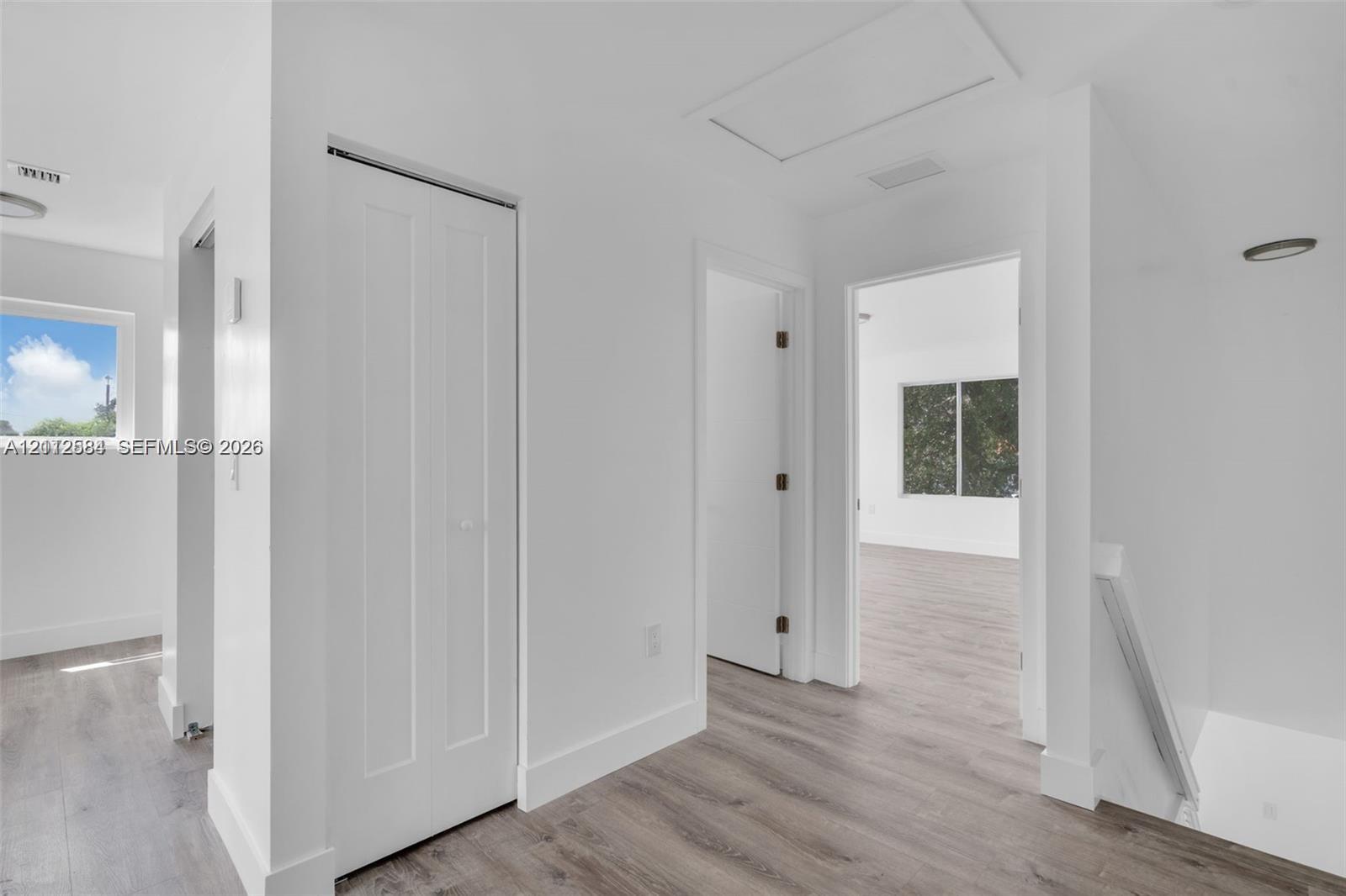 Interior hallway featuring wood-finish flooring, white walls, bi-fold closet doors, and recessed lighting