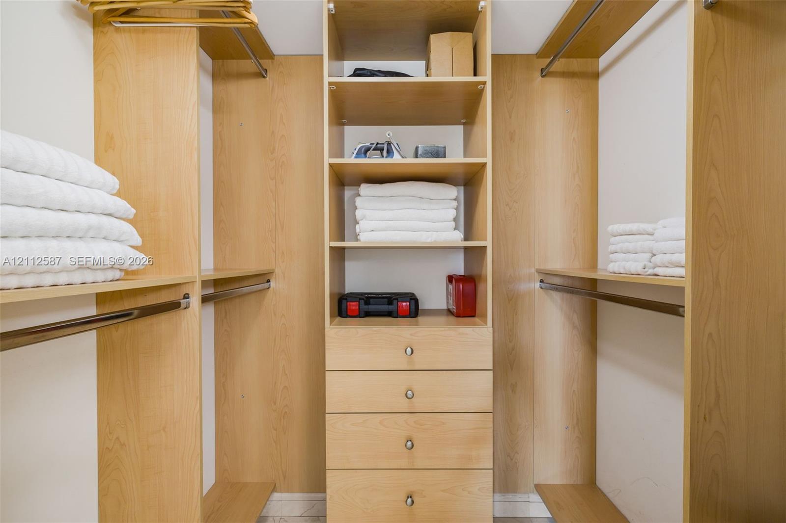 Customized closet organization system featuring light wood-finish shelving, integrated hanging rods, and a center stack of four built-in drawers