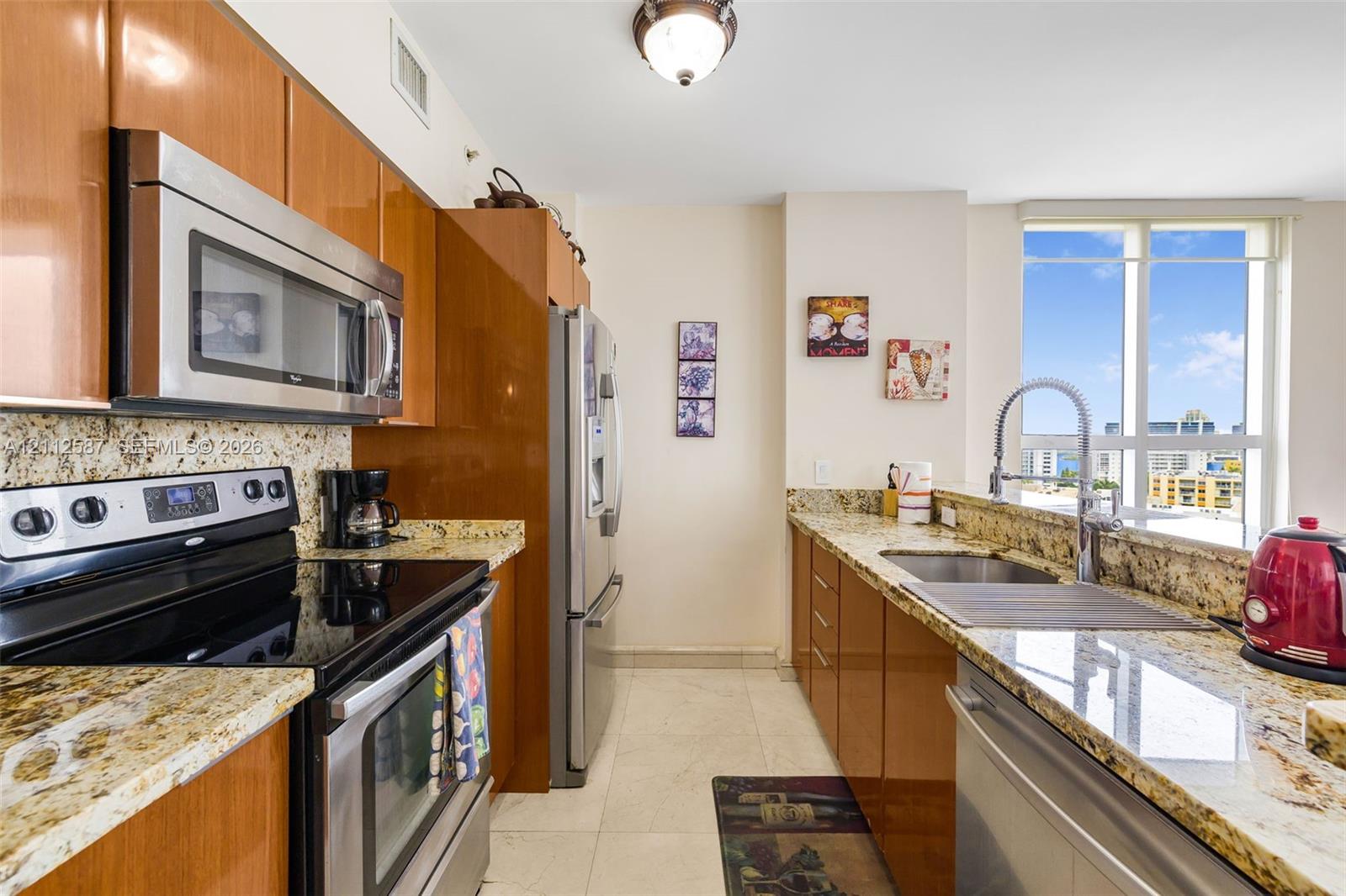 Kitchen featuring high-gloss cabinetry, stone countertops, stainless steel appliances, a high-arc pull-down faucet, and floor-to-ceiling windows