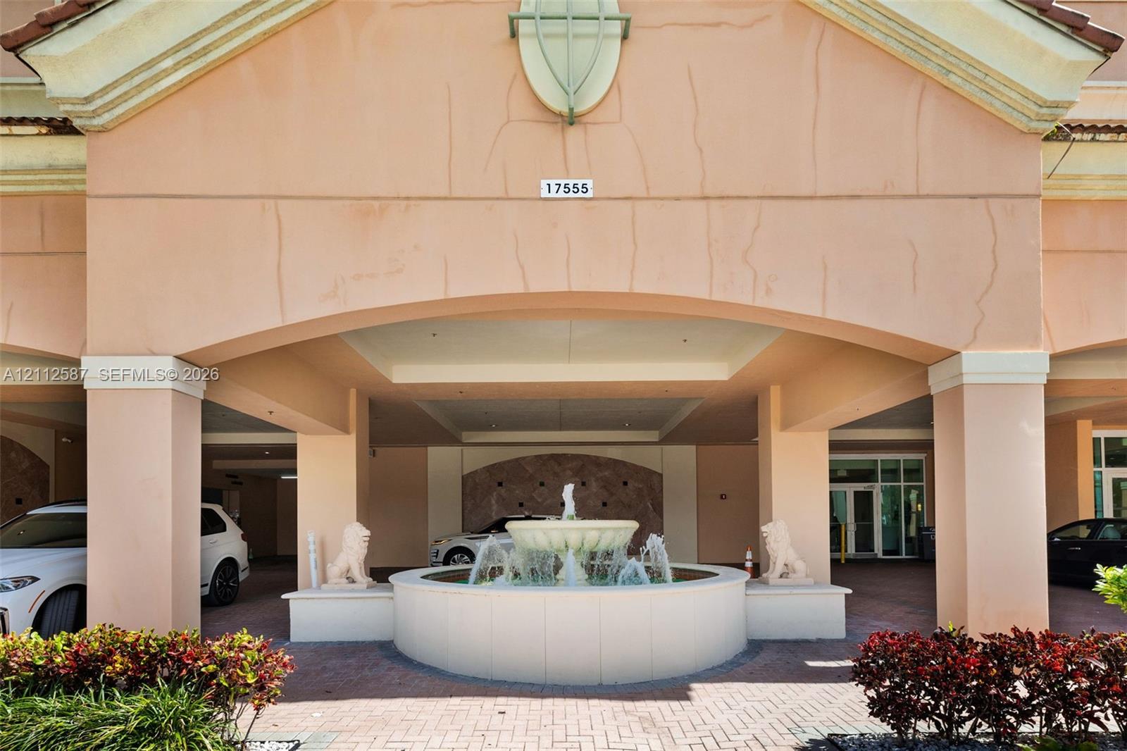 Covered entryway featuring a stone-clad portico, a central circular fountain with dual lion statues, and paver hardscaping