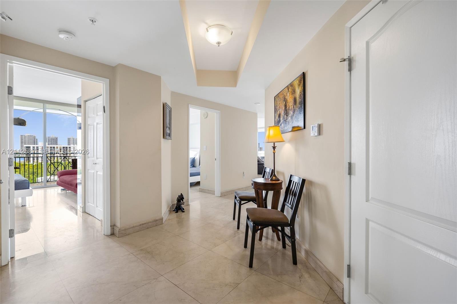 Interior hallway featuring large-format tile flooring, a recessed tray ceiling, flush-mount lighting, and solid-core interior doors