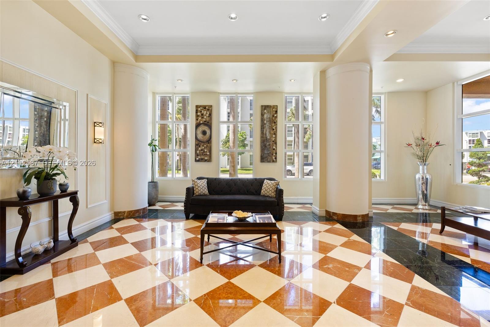 Grand lobby featuring a checkered tile floor, recessed lighting, multi-pane floor-to-ceiling windows, and structural columns with stone-finish accents