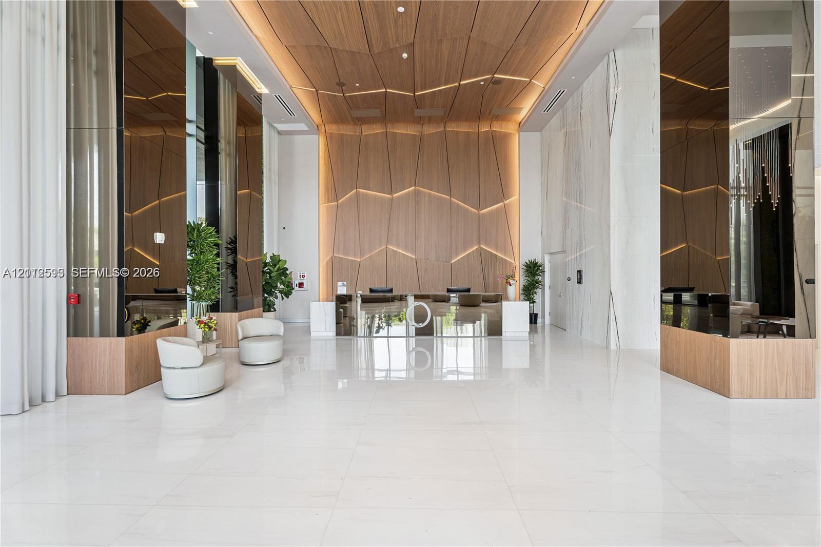Grand lobby featuring large-format tile flooring, reflective mirror-clad columns, and a geometric wood-paneled accent wall with integrated linear lighting