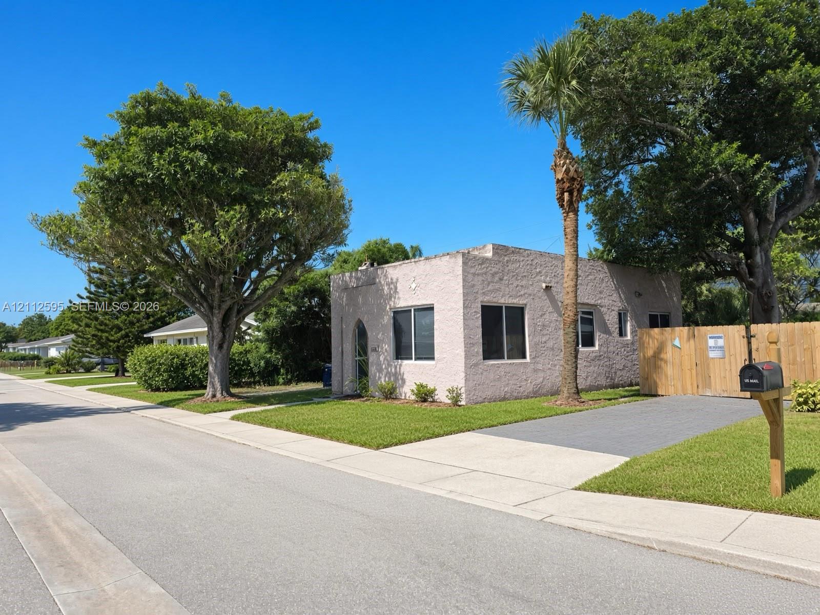Stucco exterior featuring an arched entryway, paved driveway, wood fencing, and mature landscaping