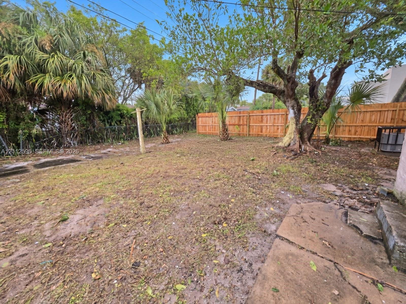 Backyard featuring a wood privacy fence, mature trees, ornamental palms, and concrete hardscaping