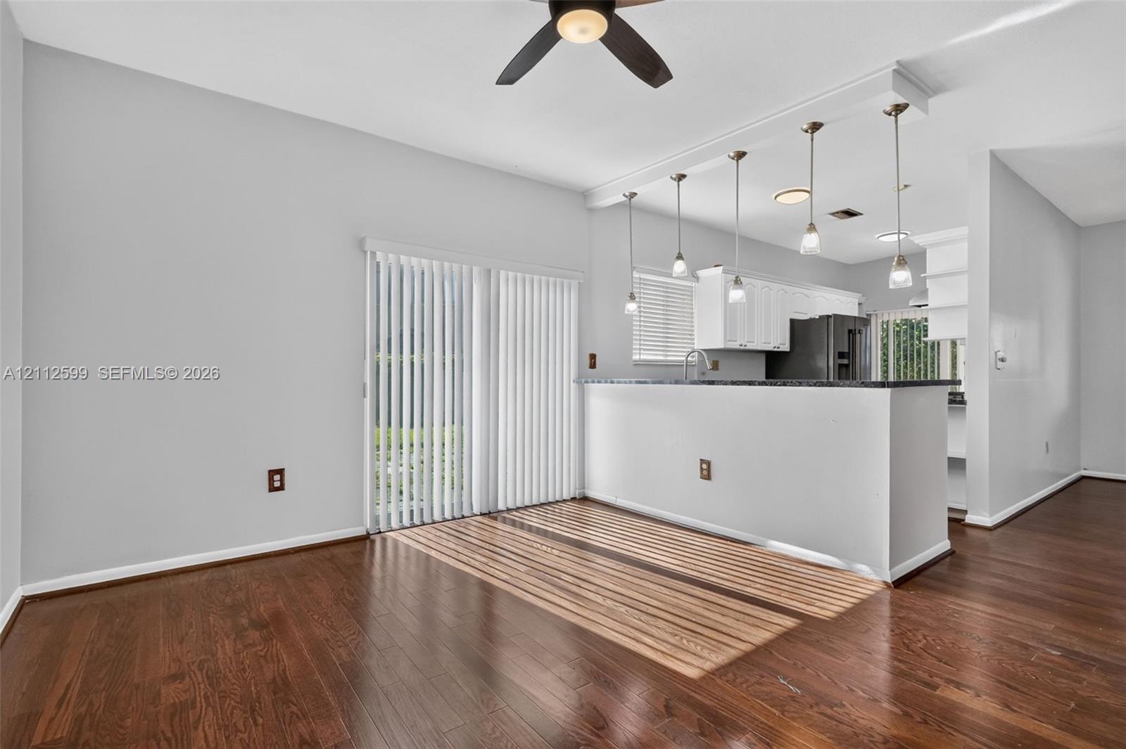 Wood-finish flooring, breakfast bar with pendant lighting, white cabinetry, and vertical window blinds