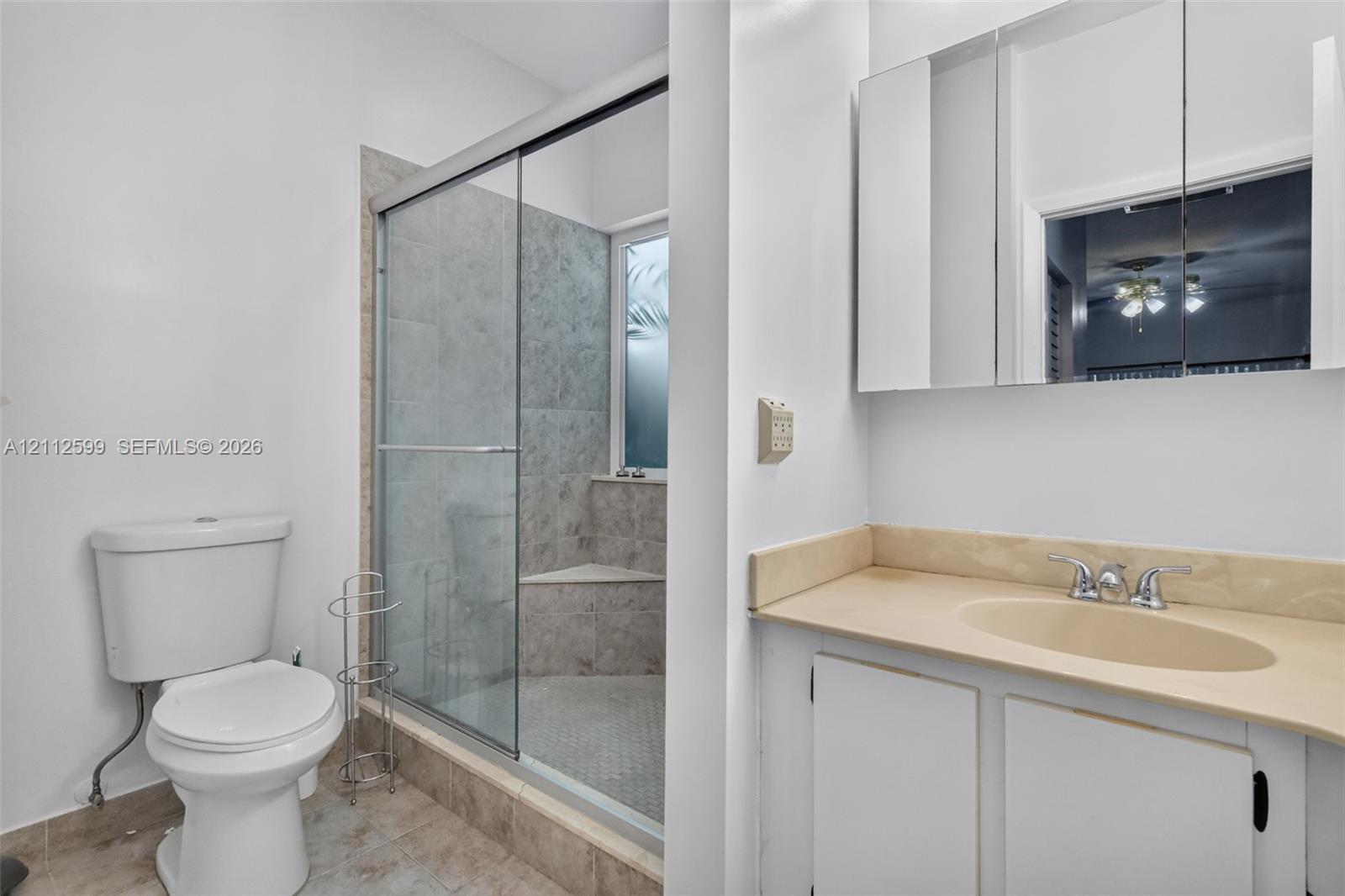Bathroom featuring a vanity with an integrated sink, neutral countertop, wall-mounted mirrored medicine cabinet, and a walk-in shower with a glass enclosure and tiled bench