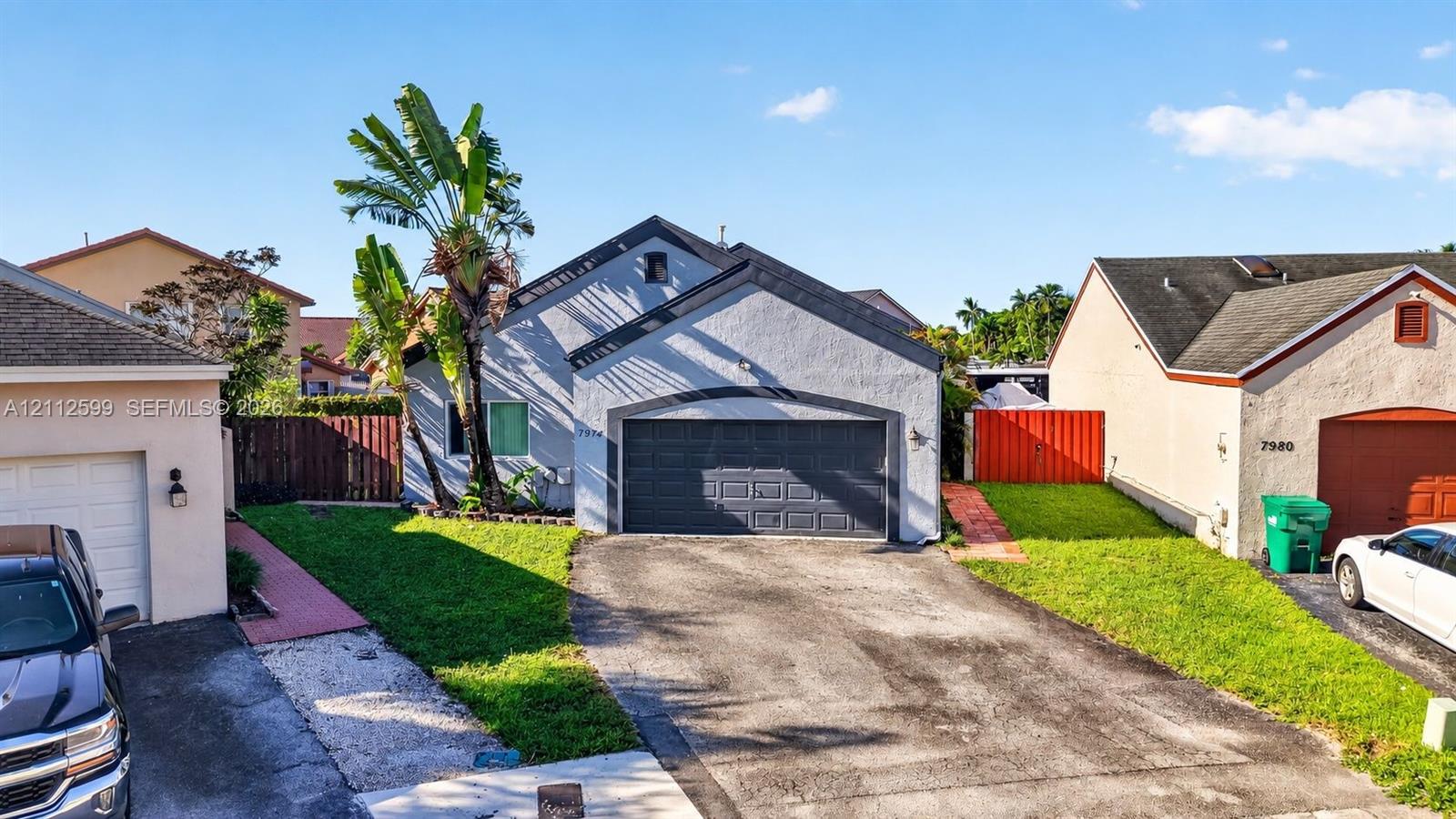 Stucco exterior residence featuring an asphalt shingle roof, a two-car garage, an asphalt driveway, and mature landscaping