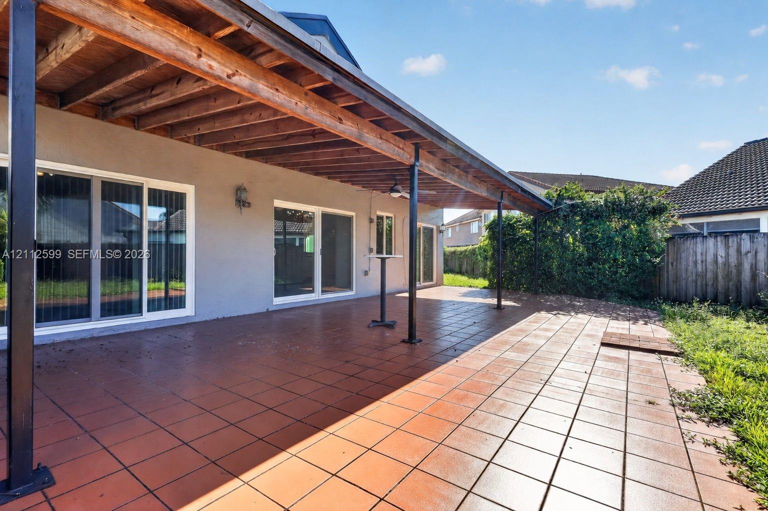 Covered patio featuring ceramic tile flooring, exposed wood ceiling beams, metal support columns, and multiple sliding glass doors