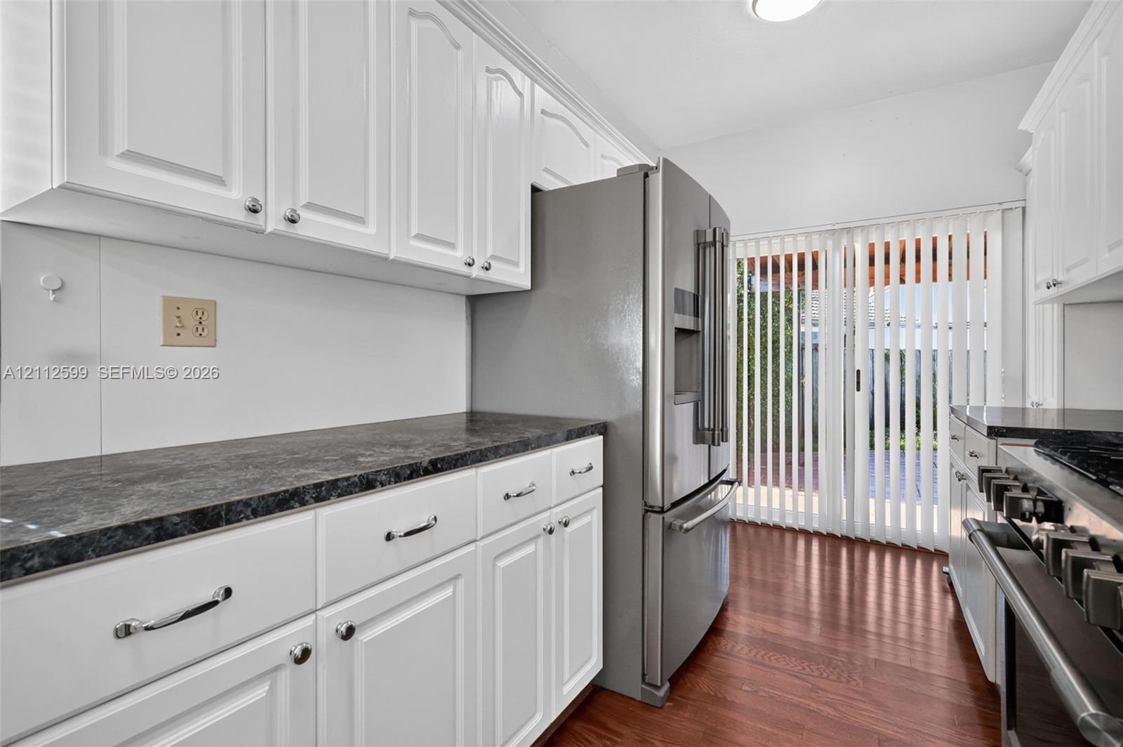 Kitchen featuring white cabinetry, dark countertops, wood-finish flooring, stainless steel refrigerator, and sliding glass doors