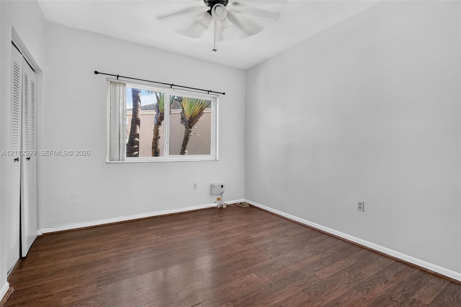 Room featuring wood-finish flooring, a ceiling fan with integrated lighting, a sliding door closet, and a window with a curtain rod