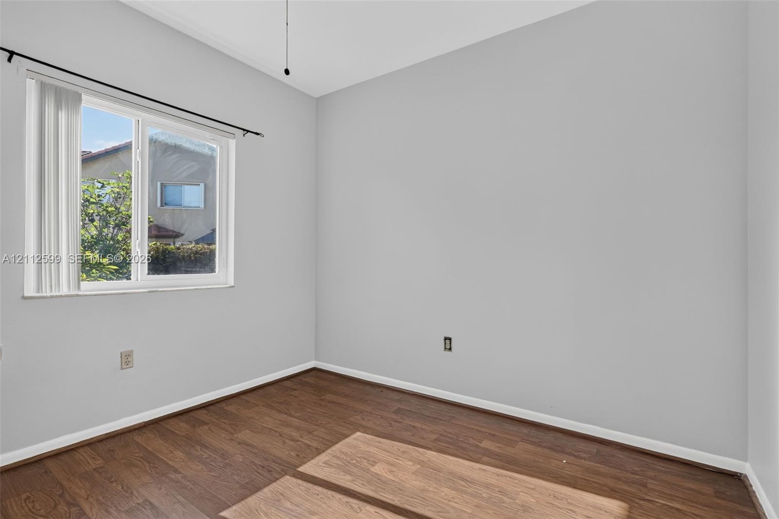 Room featuring neutral wall tones, wood-finish flooring, and a single-pane sliding window