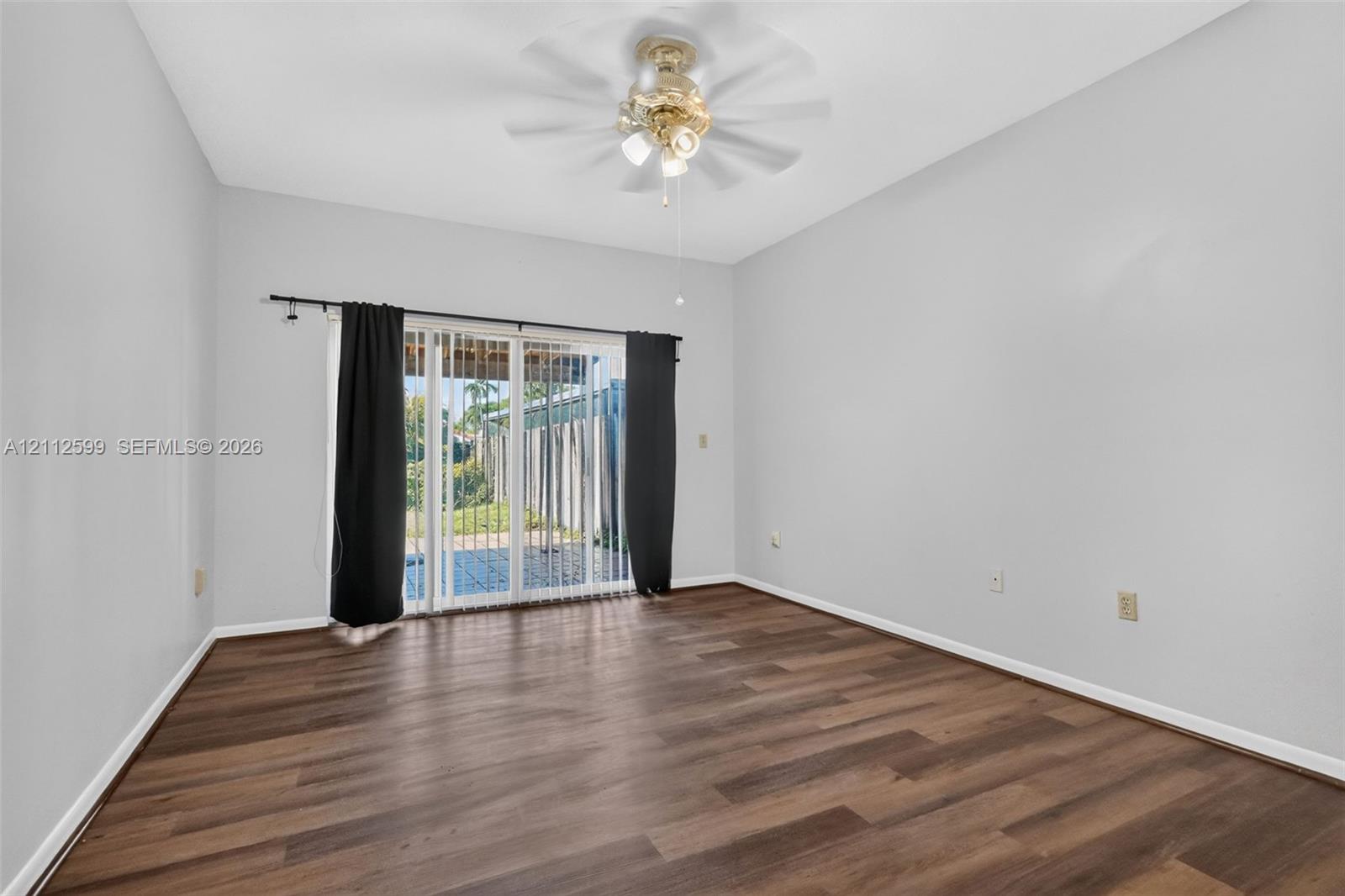 Room featuring wood-finish flooring, sliding glass doors, and a ceiling-mounted light fixture with a multi-blade fan