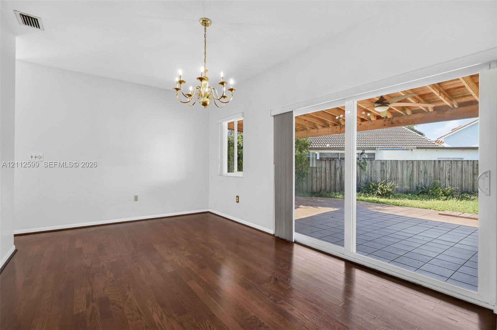 Wood-finish flooring, multi-light chandelier, sliding glass door, and exterior paved patio with wood pergola