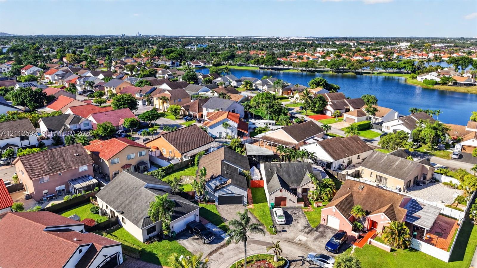 Aerial perspective of a residential neighborhood featuring multi-pitch roofs, paved driveways, manicured lawns, and proximity to a large community lake