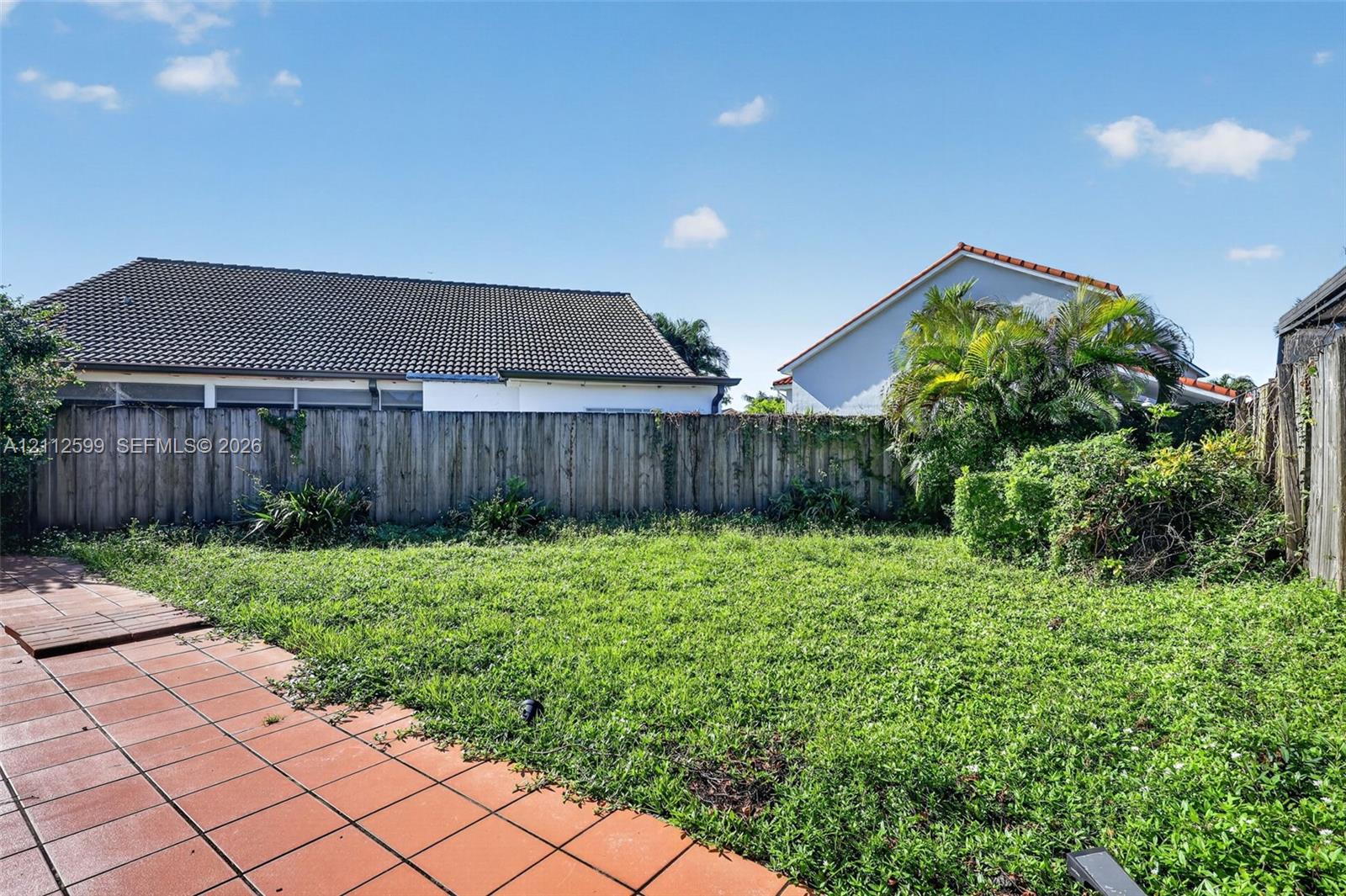 Rear exterior featuring a fenced perimeter, expansive lawn, and terracotta-style tiled patio