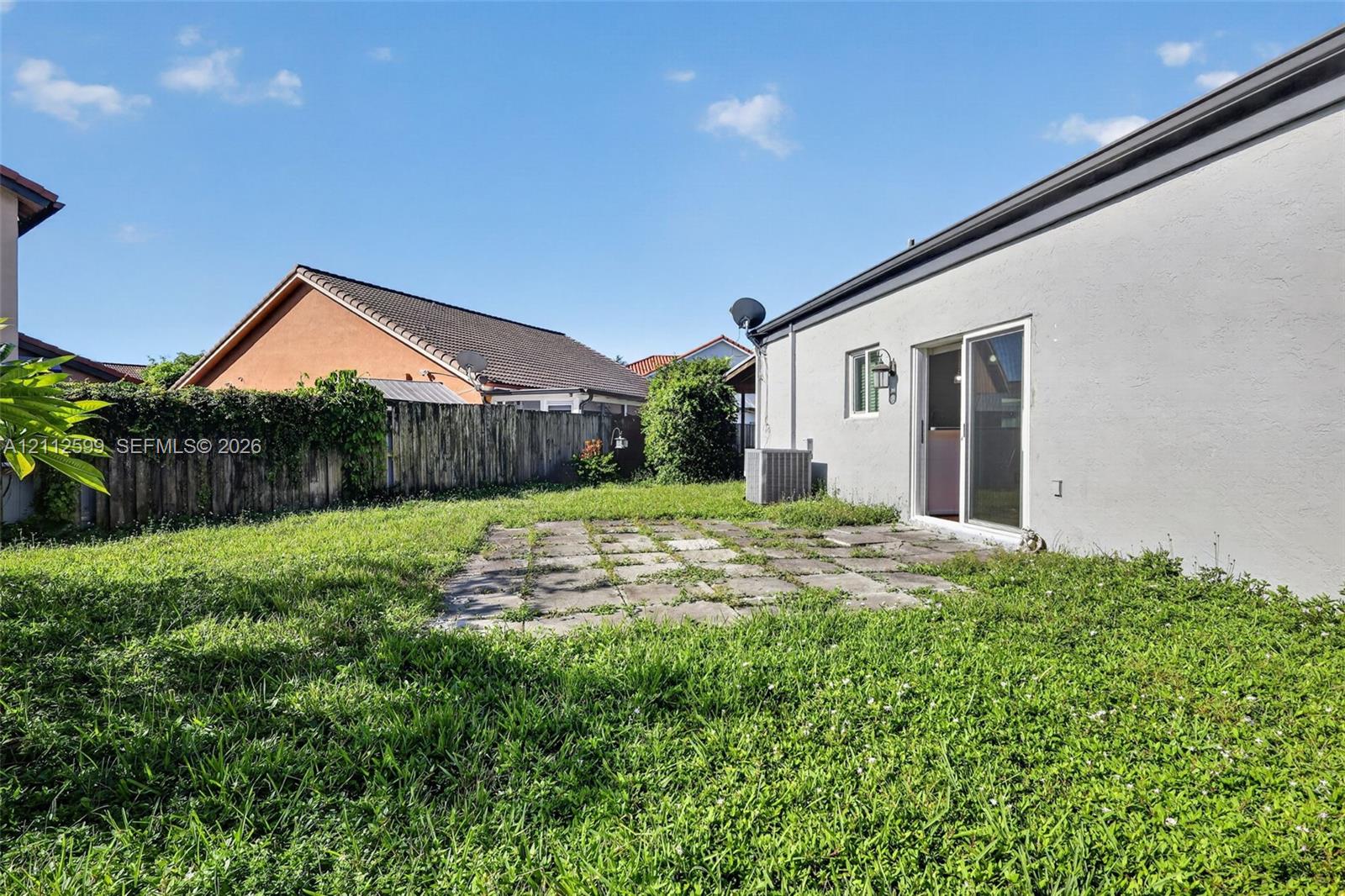 Rear exterior featuring a concrete patio, stucco siding, sliding glass door, and a wooden privacy fence