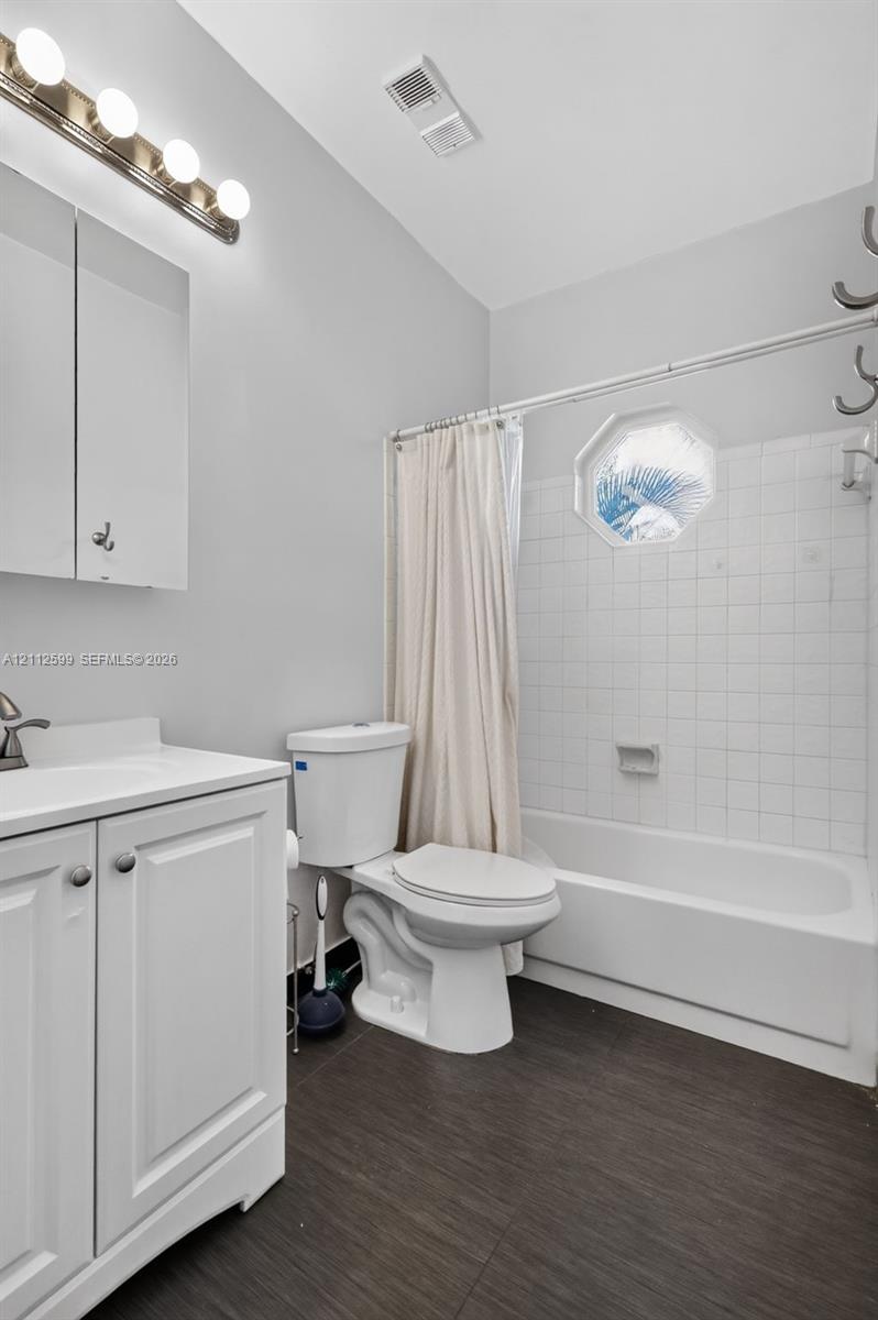 Bathroom featuring a white vanity cabinet, four-light vanity fixture, bathtub with tiled surround, and octagonal window