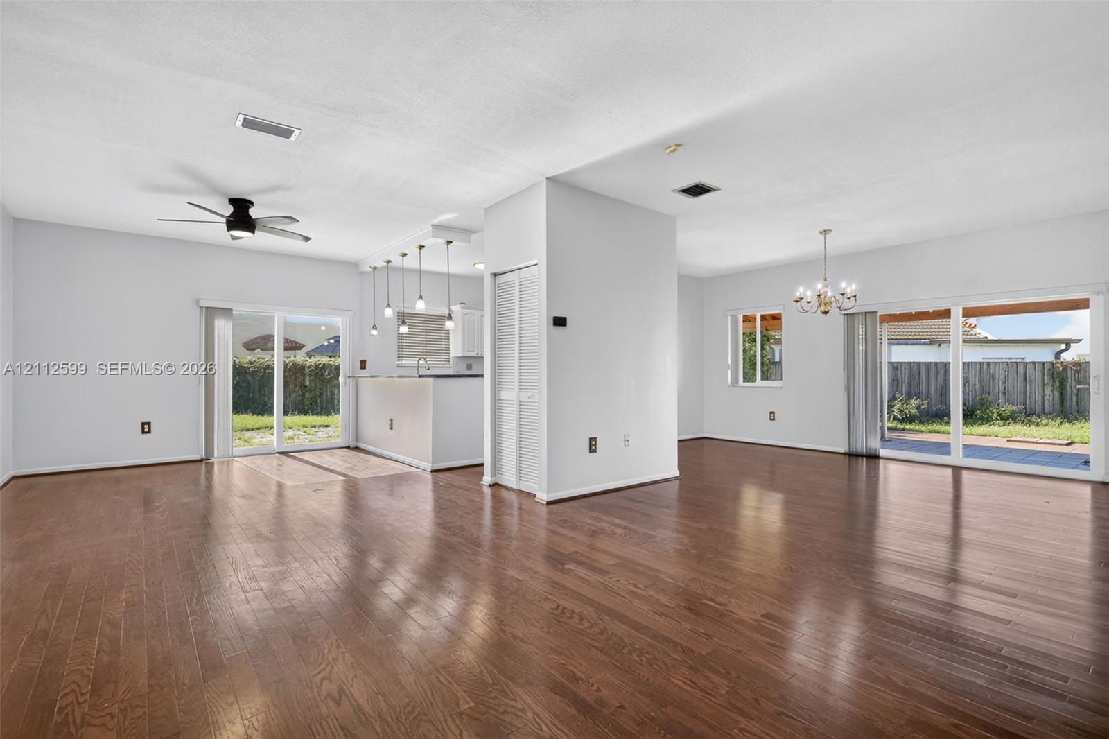 Open interior space featuring wood-finish flooring, two sets of glass sliding doors, a central ceiling fan, and pendant lighting over a built-in counter