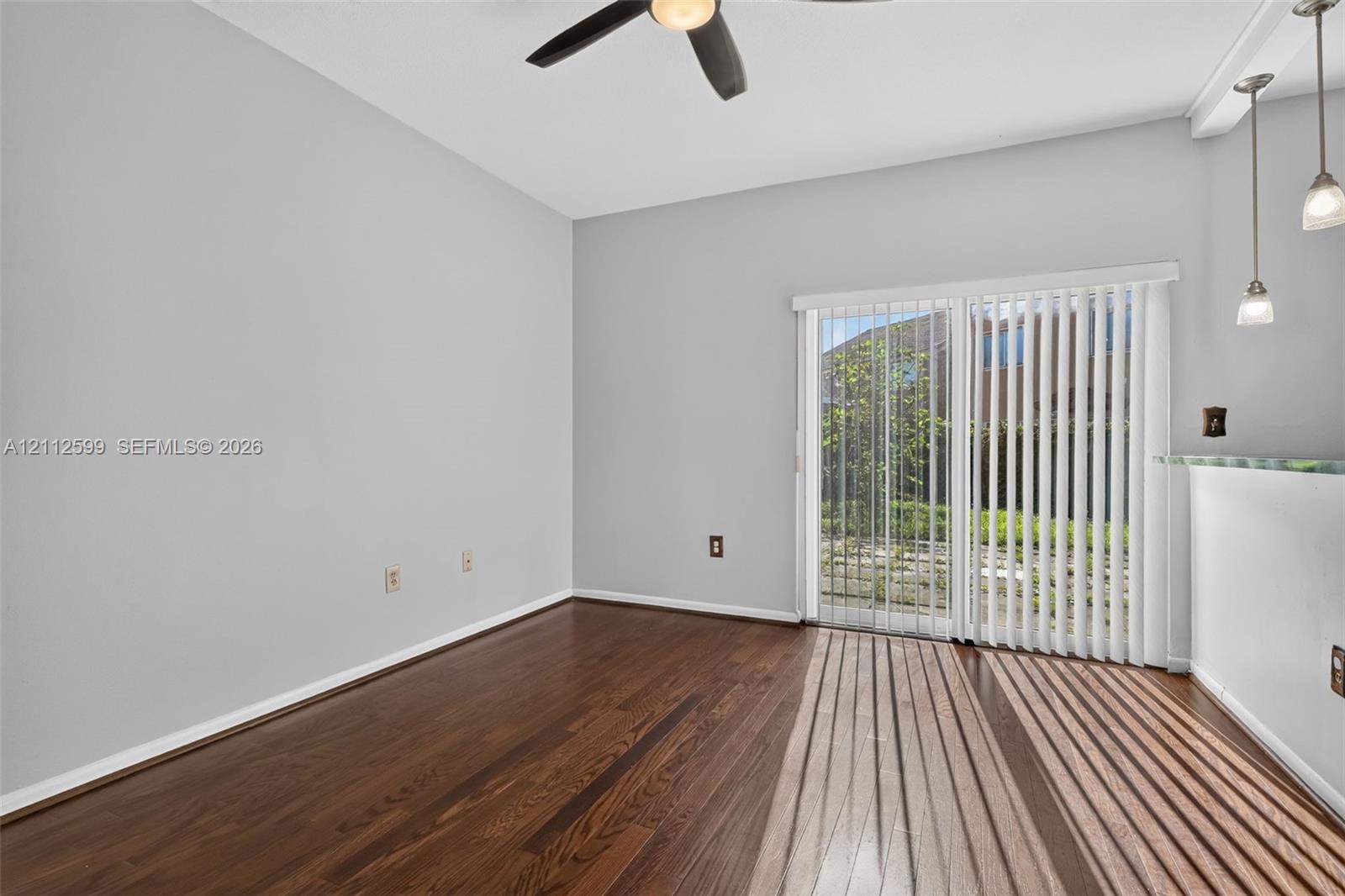 Room featuring wood-finish flooring, sliding glass doors with vertical blinds, a ceiling fan, and pendant lighting