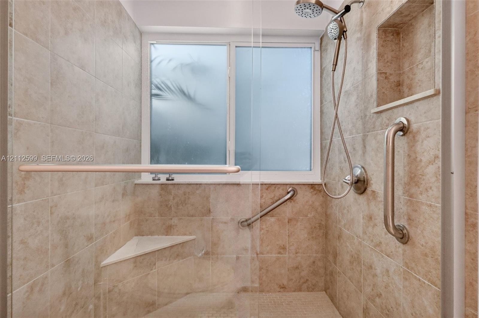 Walk-in shower featuring floor-to-ceiling stone-finish tile, a built-in corner bench, a recessed wall niche, a sliding shower head, and metal grab bars