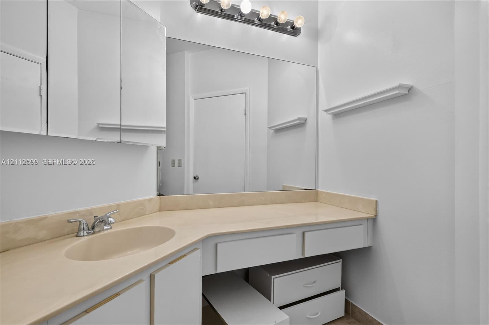 Built-in vanity featuring a solid surface countertop, integrated sink, multi-drawer storage, large wall-mounted mirror, and multi-bulb vanity light fixture