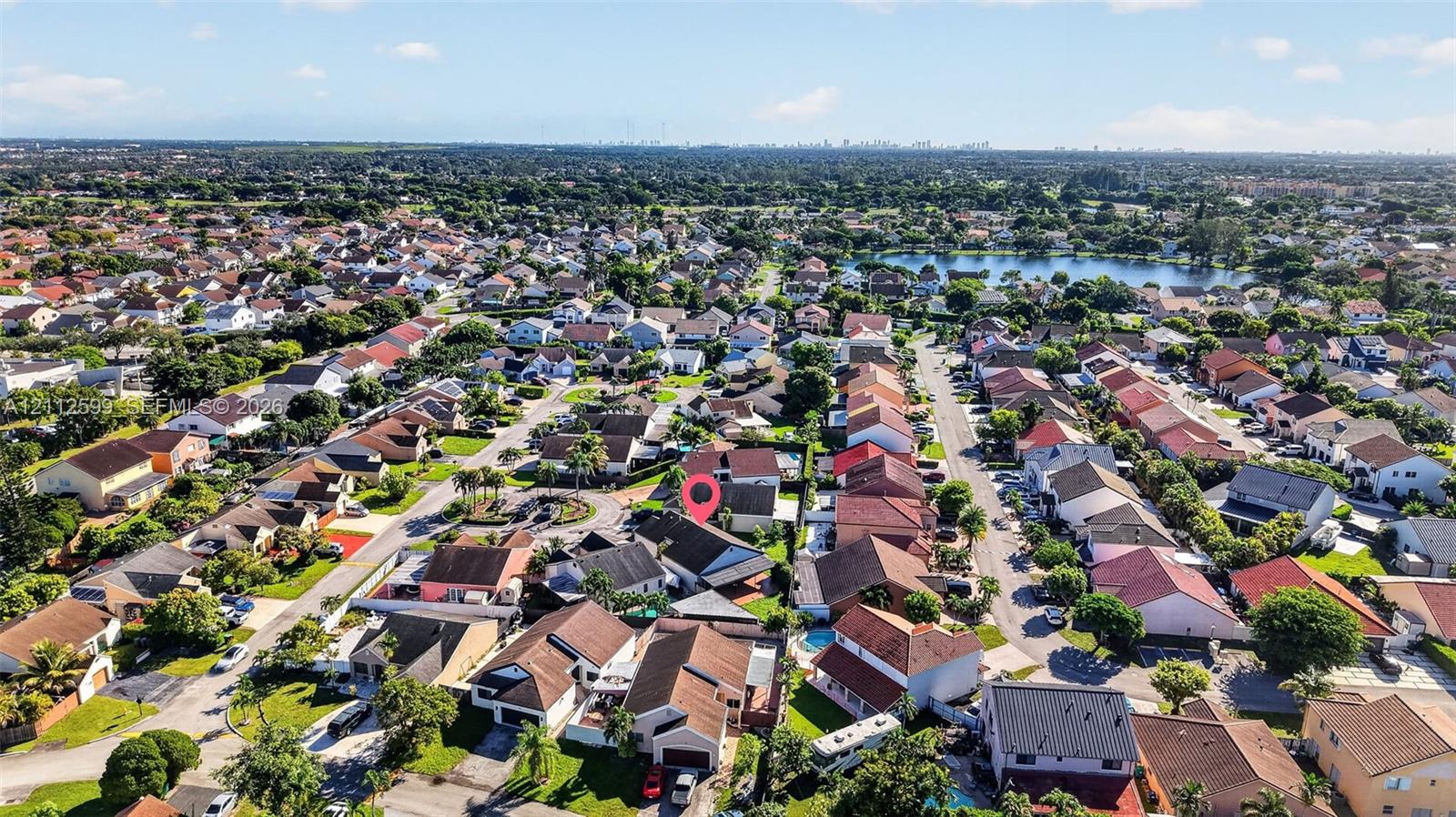 Aerial perspective of a suburban neighborhood featuring a grid-pattern street layout, dense residential housing, and a central lake