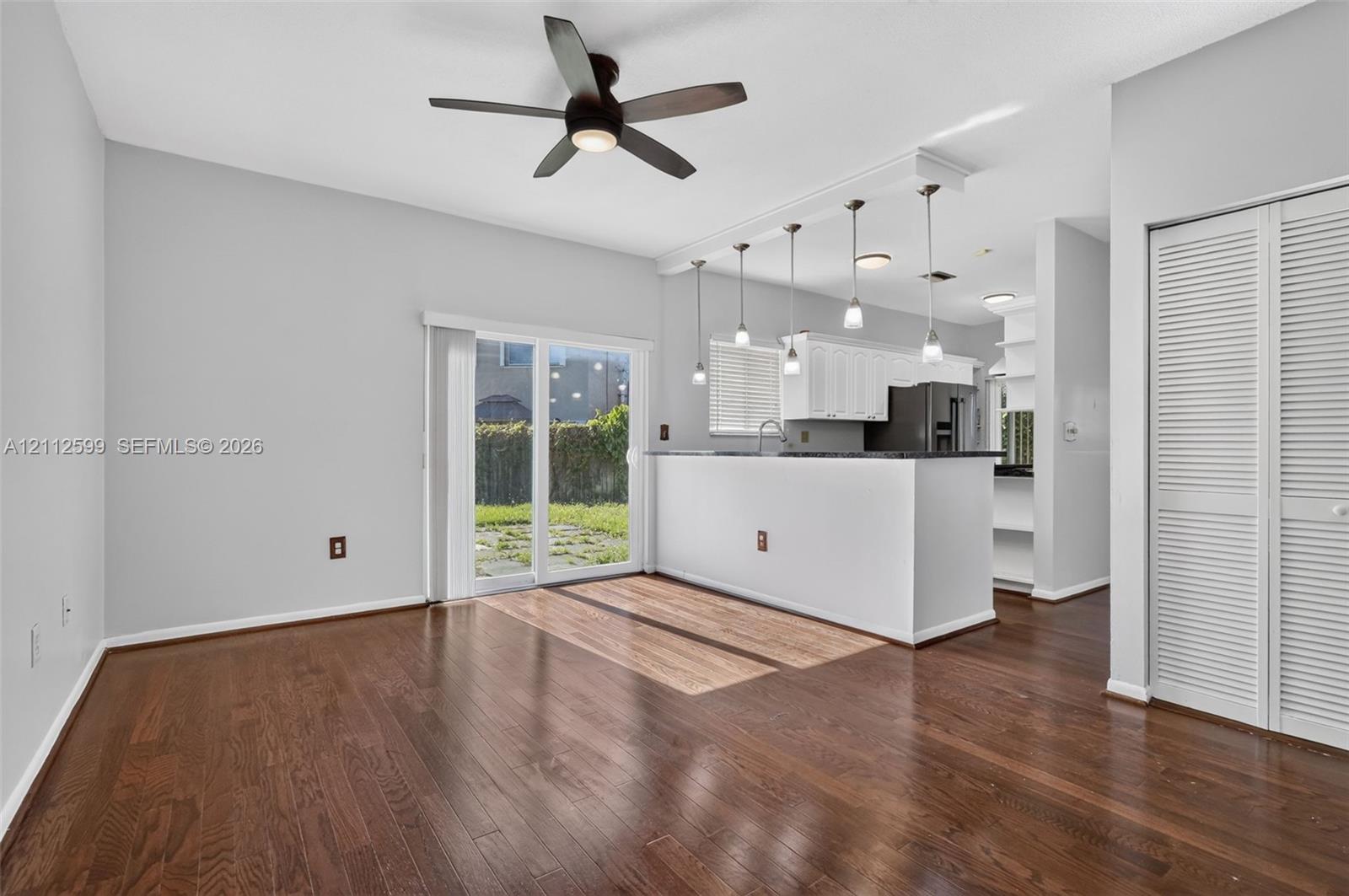 Wood-finish flooring, kitchen peninsula with pendant lighting, sliding glass door, white louvered closet doors, and ceiling fan with integrated light