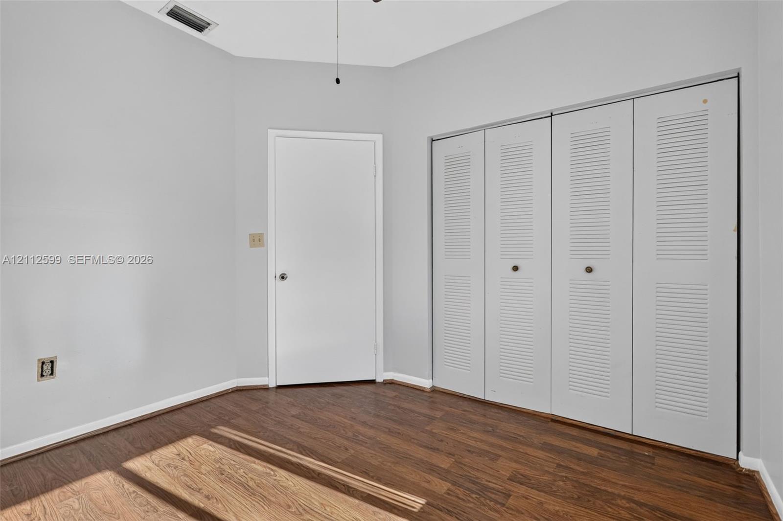 Interior room featuring wood-finish flooring, neutral wall paint, and floor-to-ceiling closet cabinetry with white louvered bifold doors