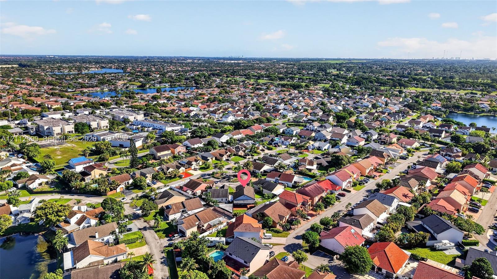 Aerial perspective of a suburban neighborhood featuring a residential lot with a peaked roof structure, paved driveway, and established tree canopy